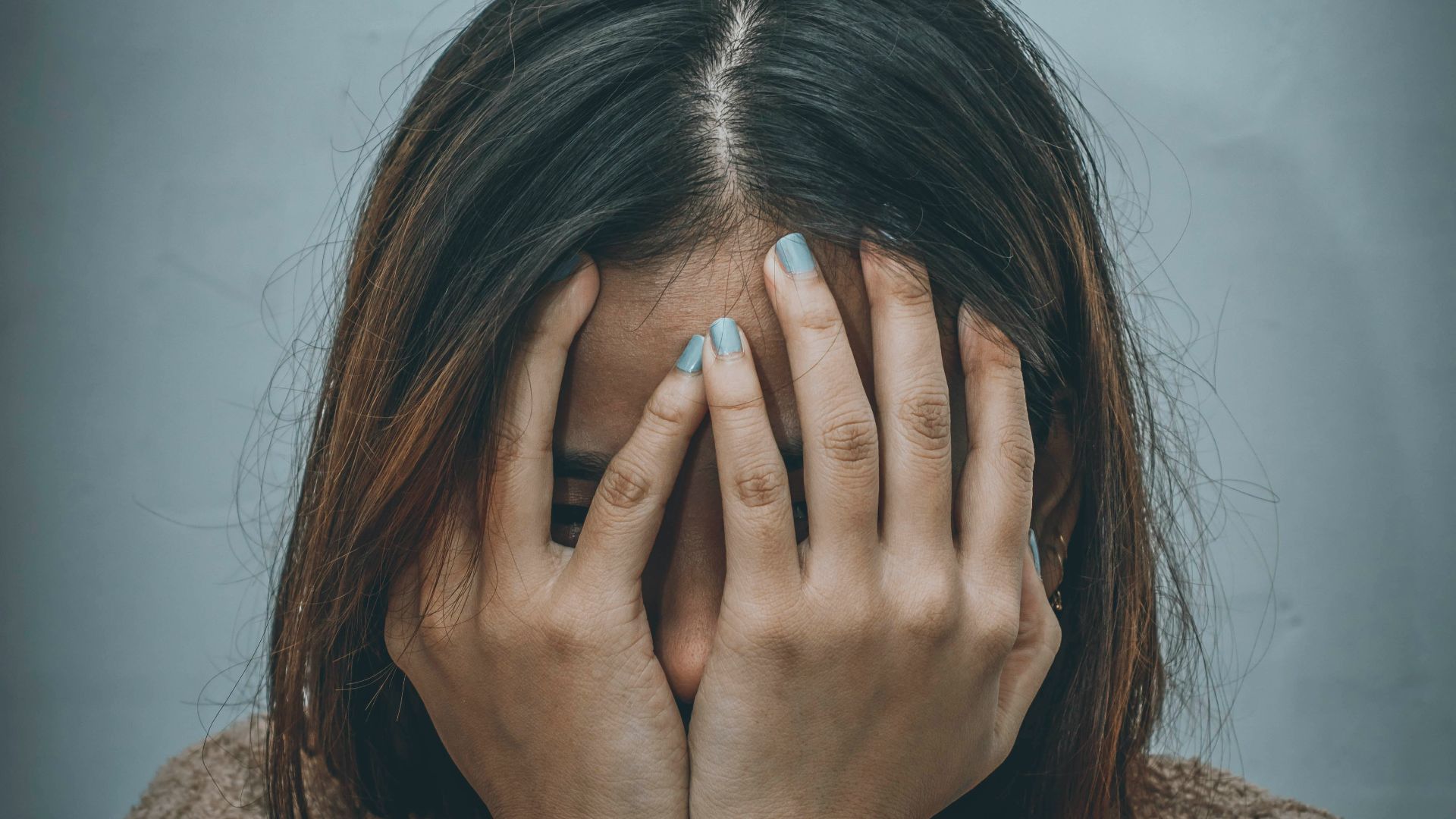 woman in brown sweater covering her face with her hand