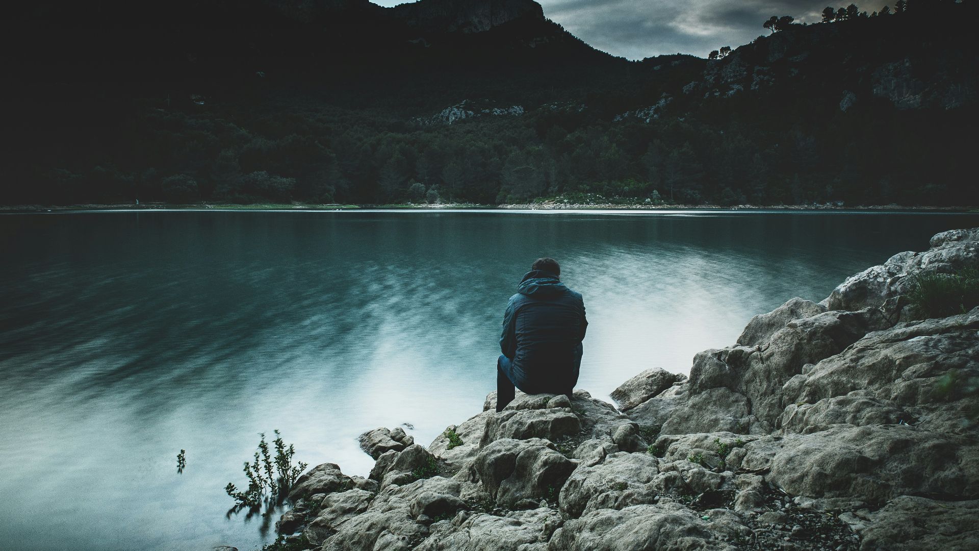 a man sits on a rock staring across a lake at dusk
