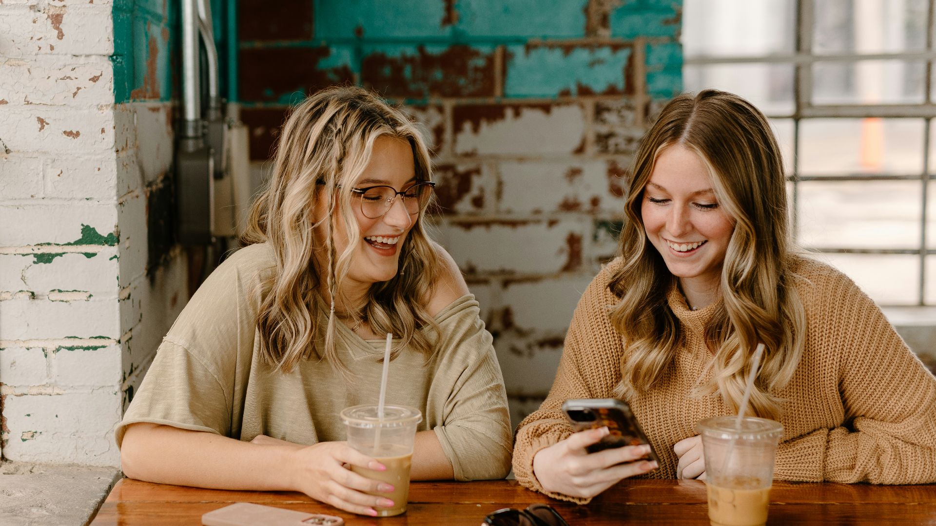two women sitting at a table looking at a cell phone