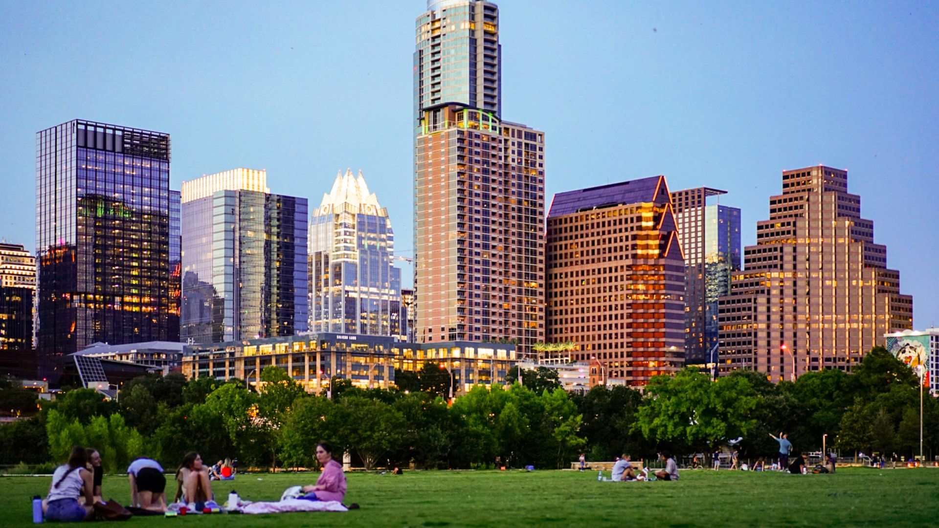 people sitting on green grass field near city buildings during daytime