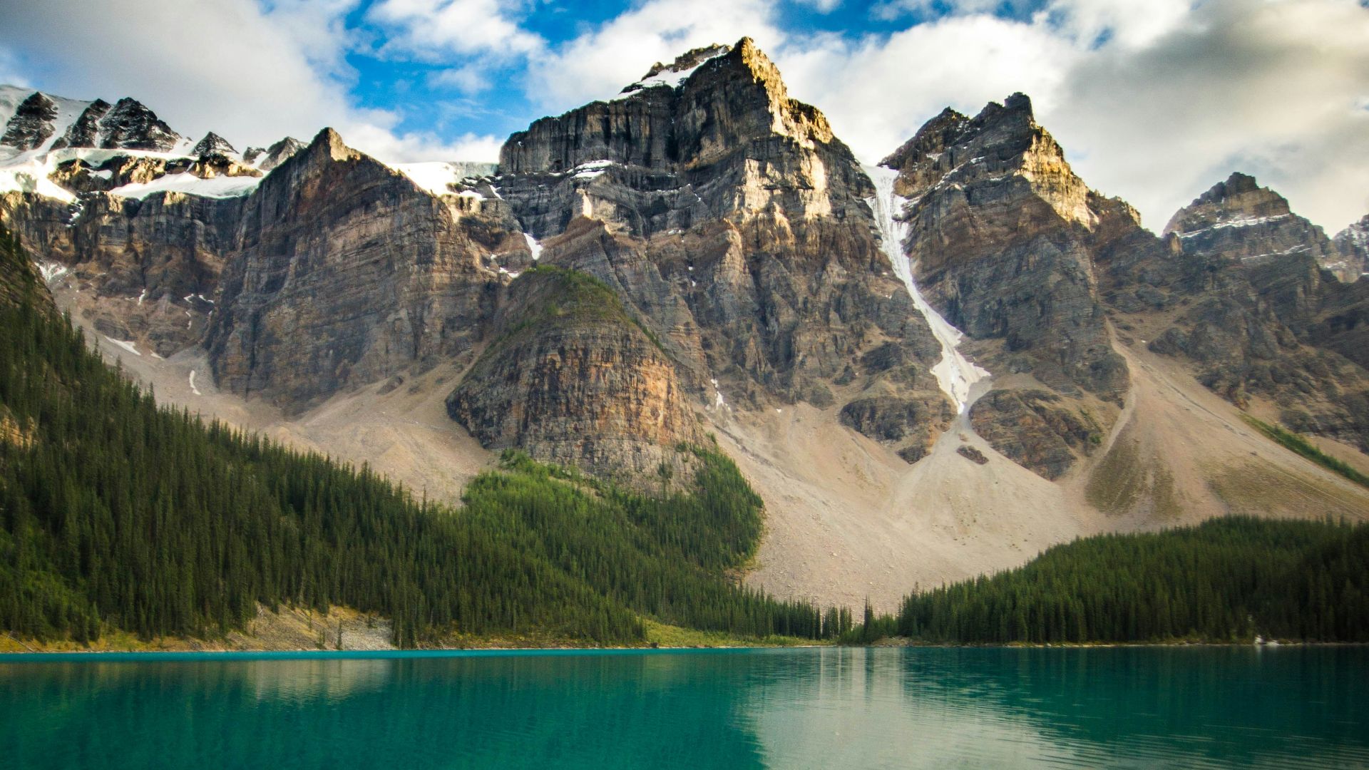 a lake surrounded by mountains under a cloudy sky