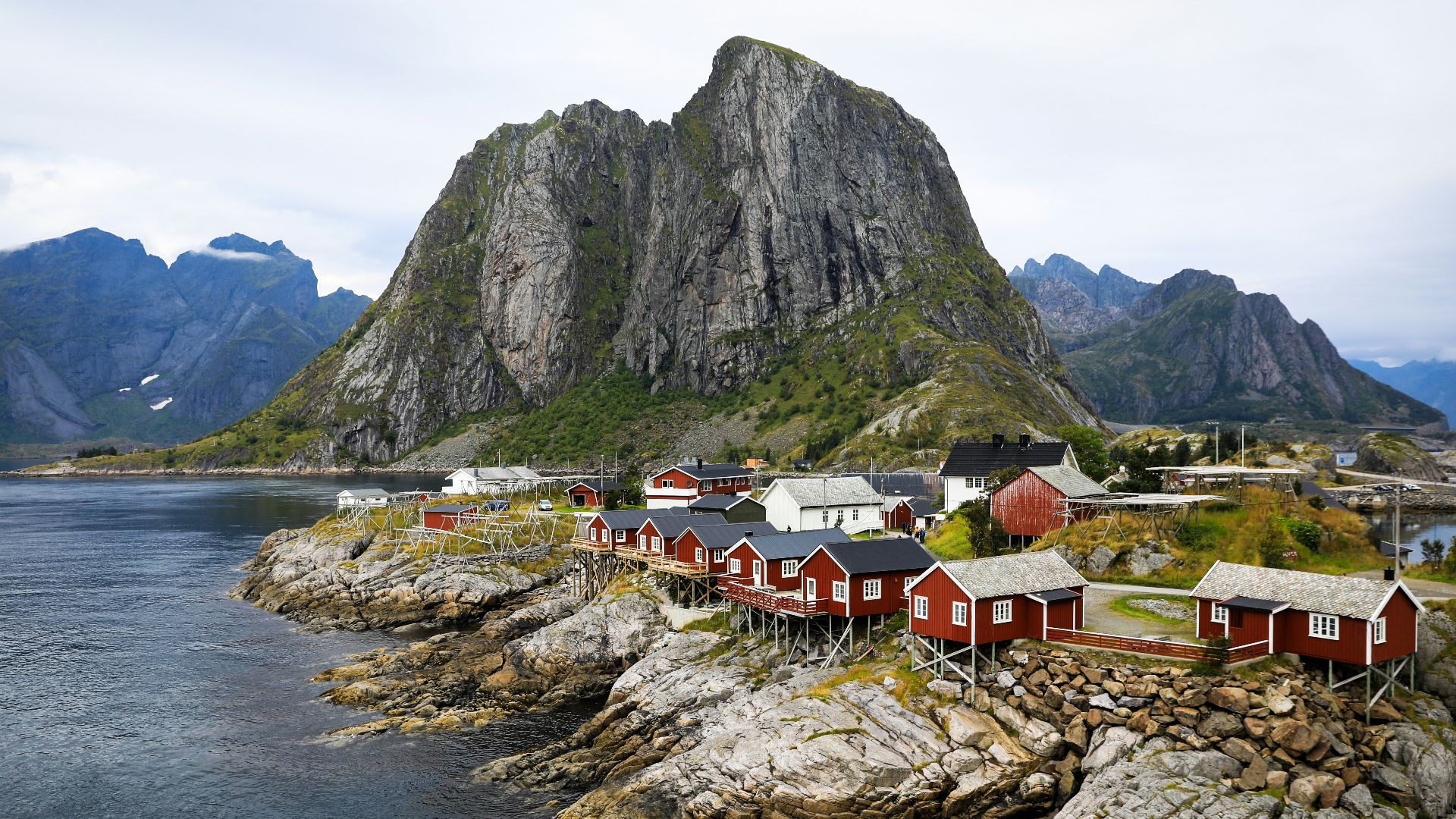 a group of houses by a body of water with mountains in the background with Lofoten in the background