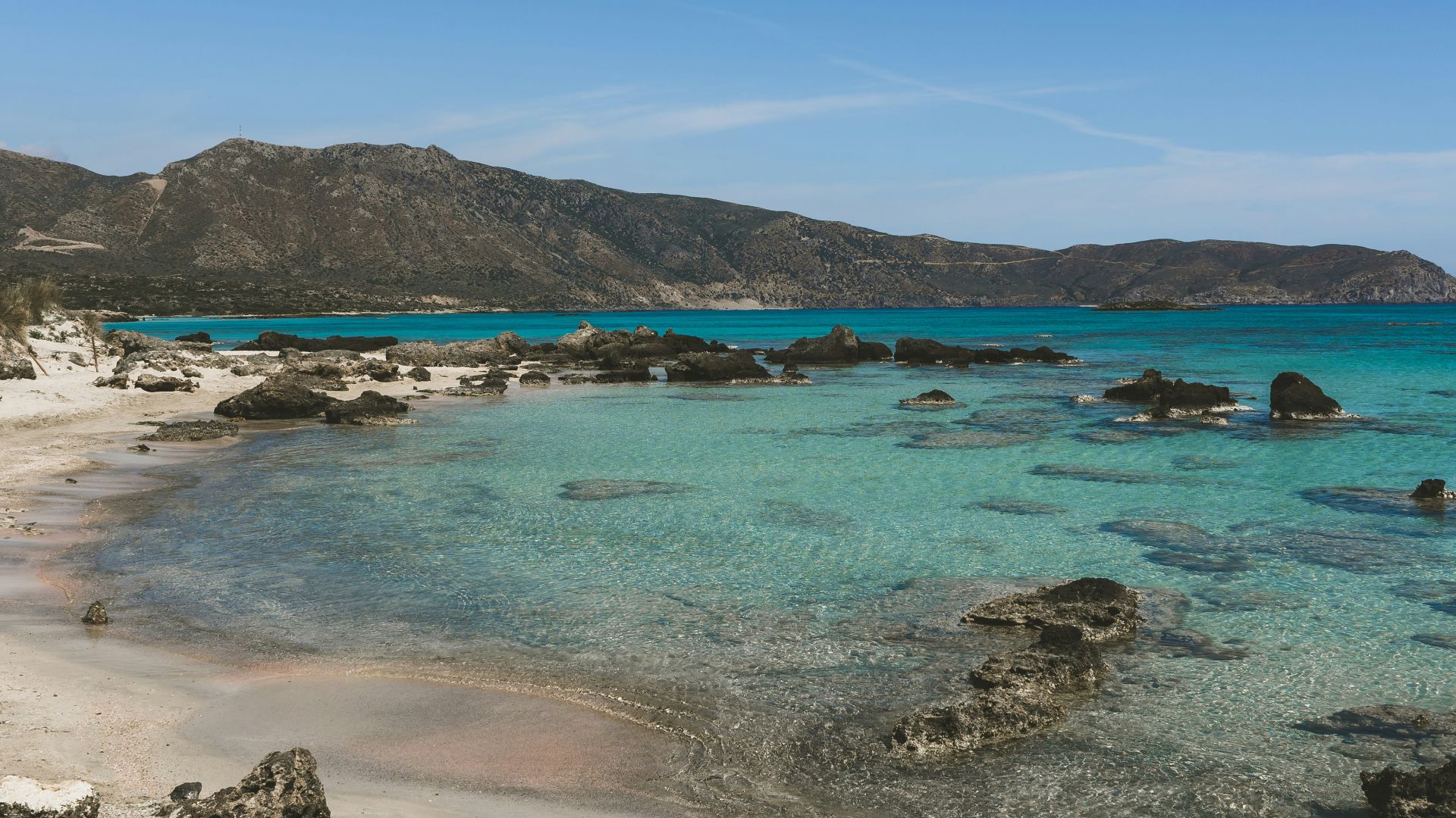 a sandy beach with clear blue water and mountains in the background