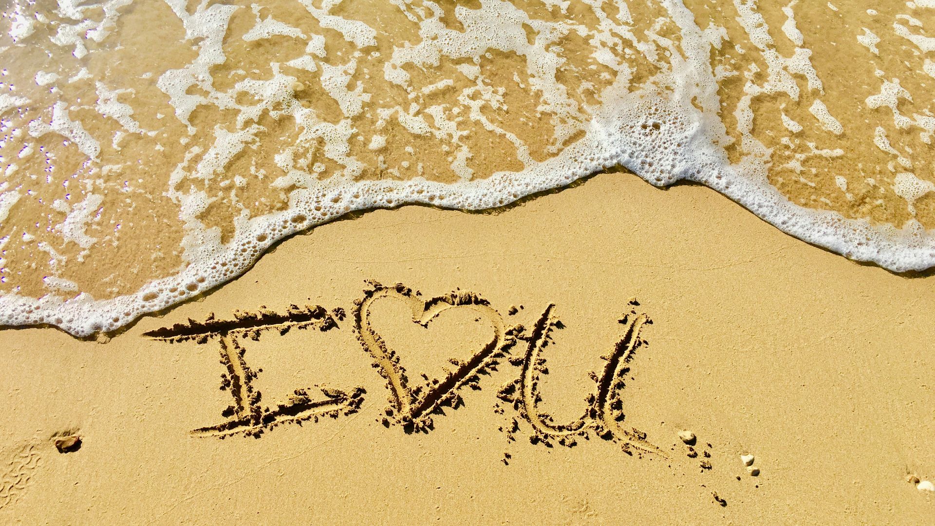 aerial photo of I love you text on sand at the seashore
