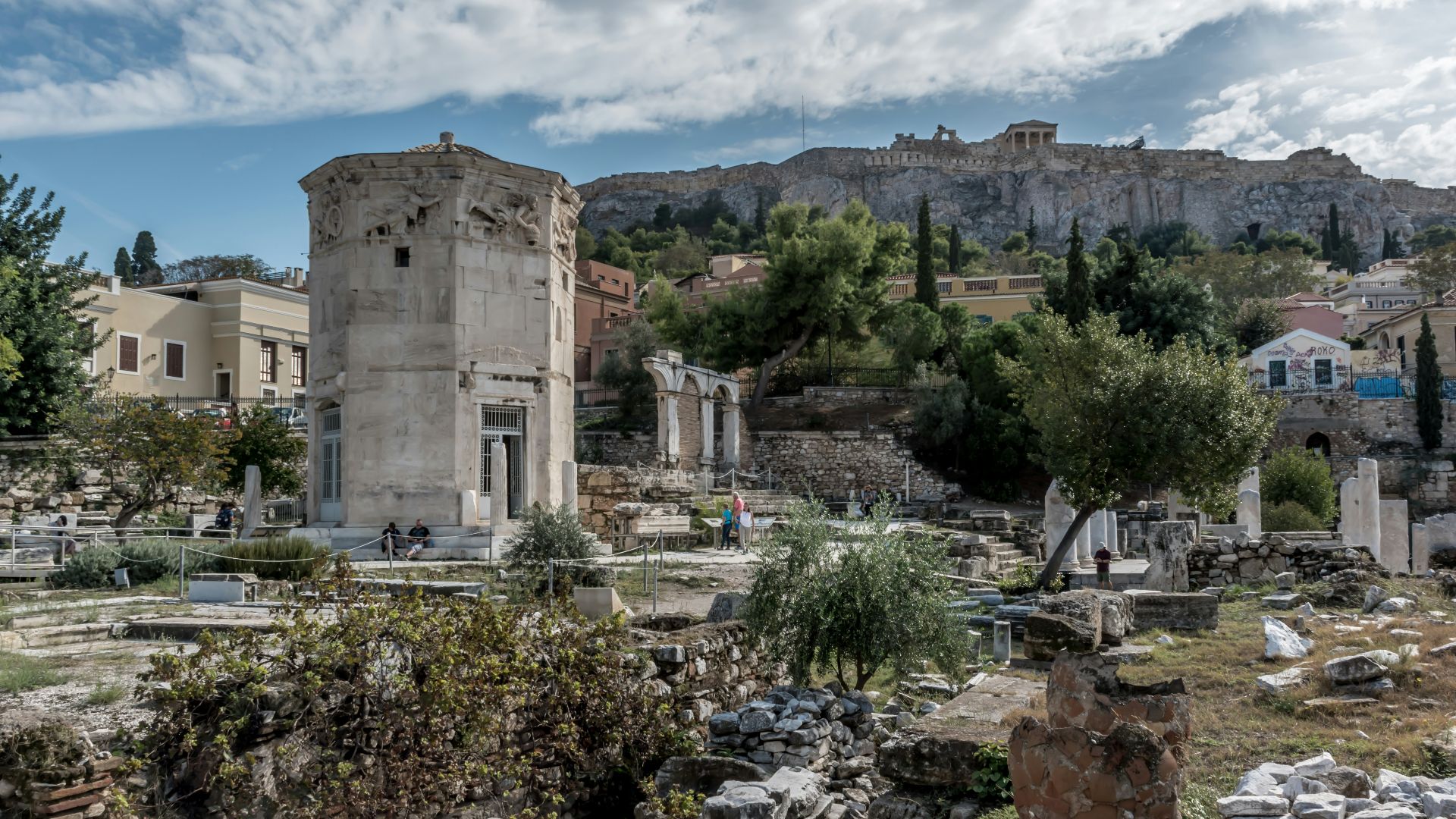 brown concrete building near green trees under white clouds and blue sky during daytime
