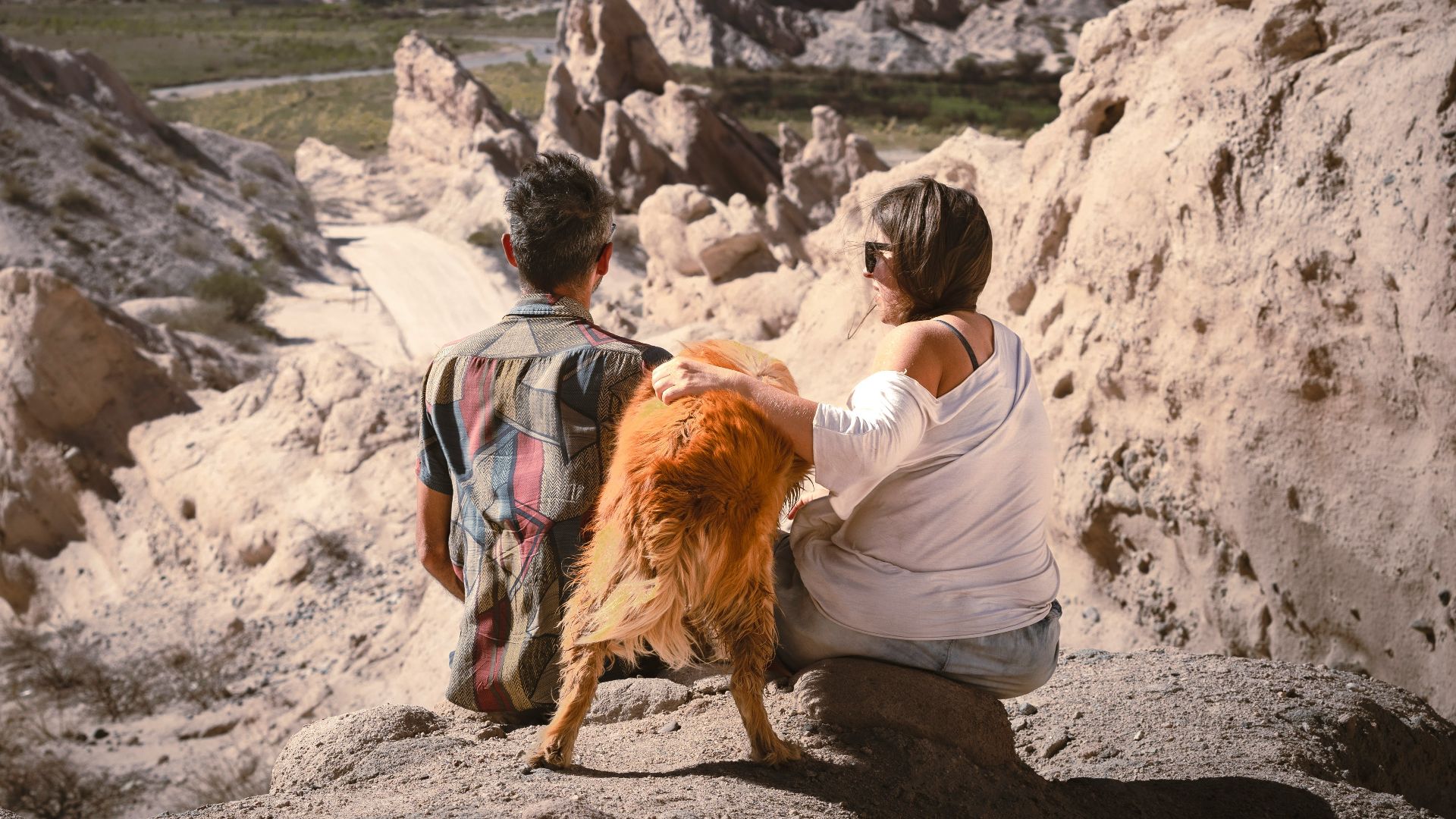 a man and a woman sitting on a rock with a dog