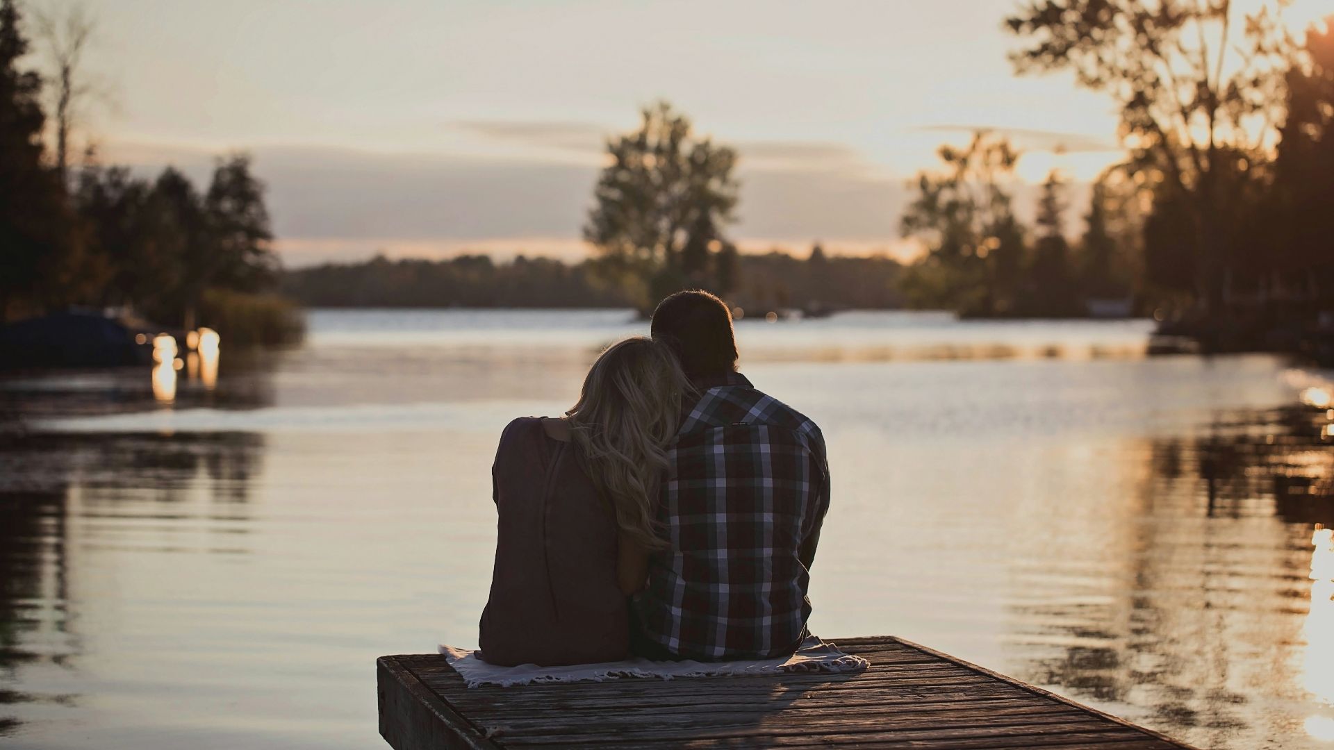 man and woman sitting on dock during golden hour