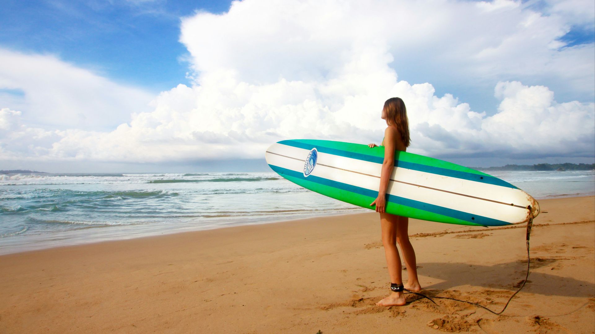 woman standing near sea holding white, blue, and green surfboard under blue sky