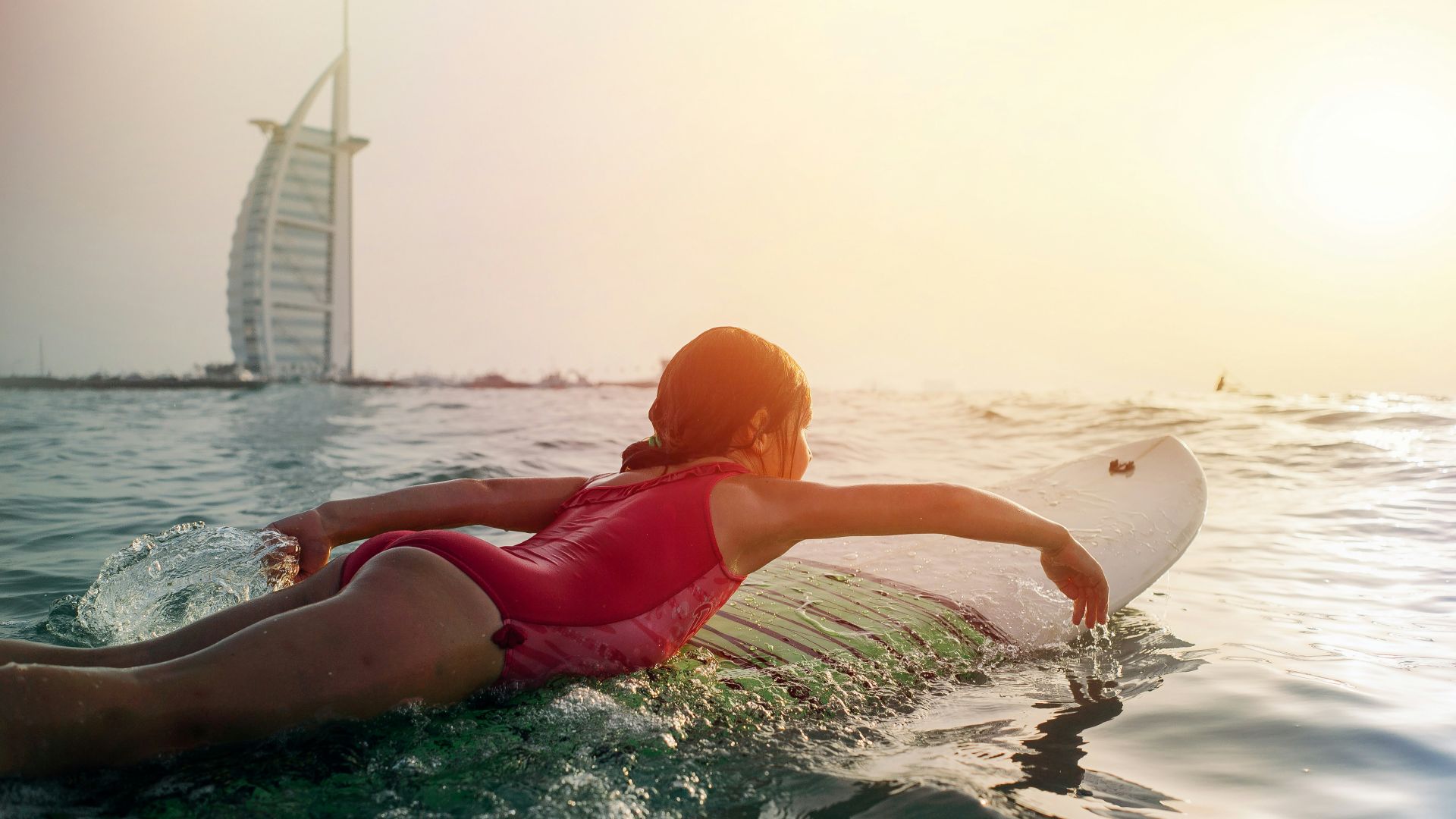 girl on top of white surfboard beside Burj Al Arab