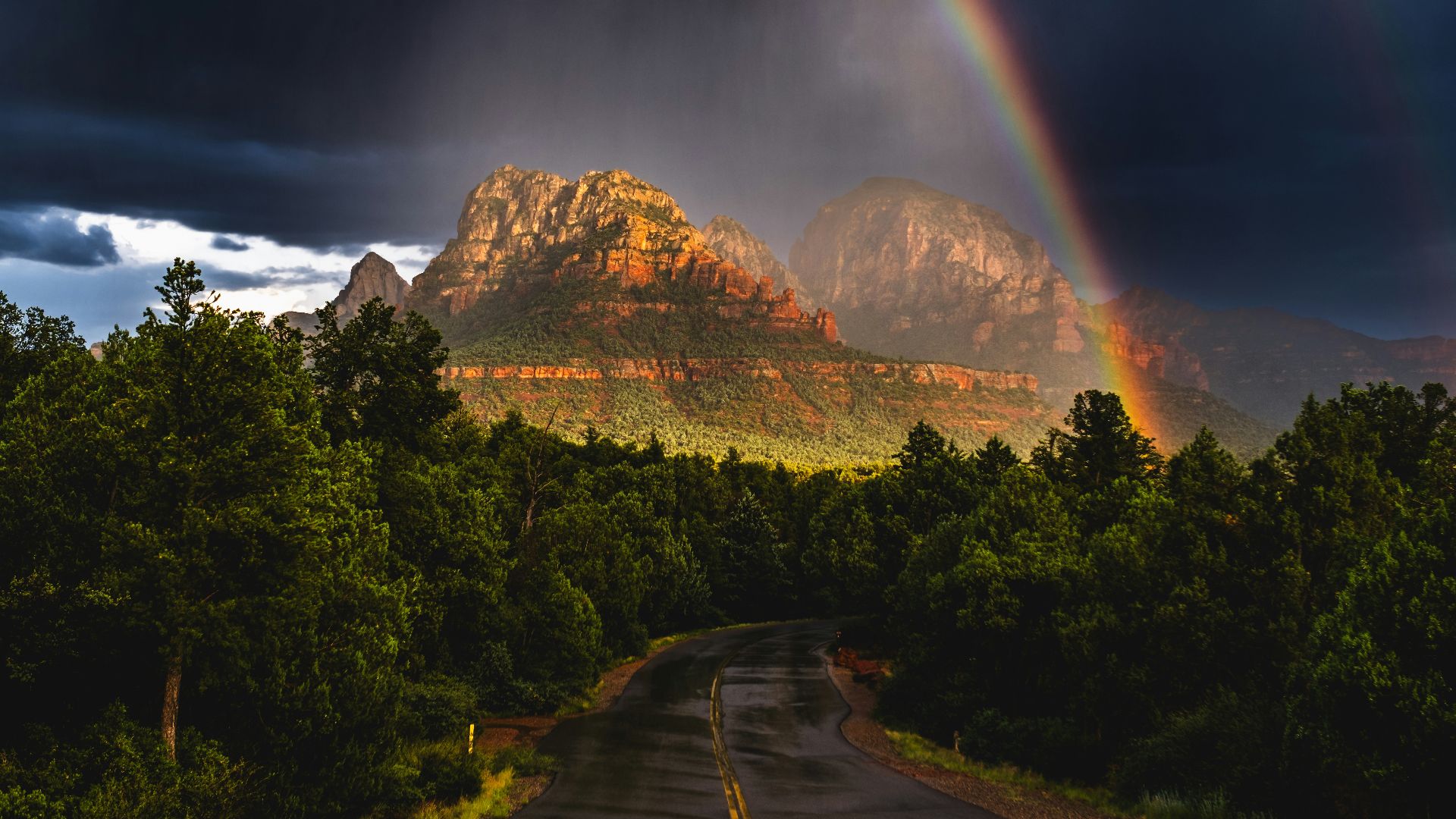 A rainbow appears over a road with a mountain in the background