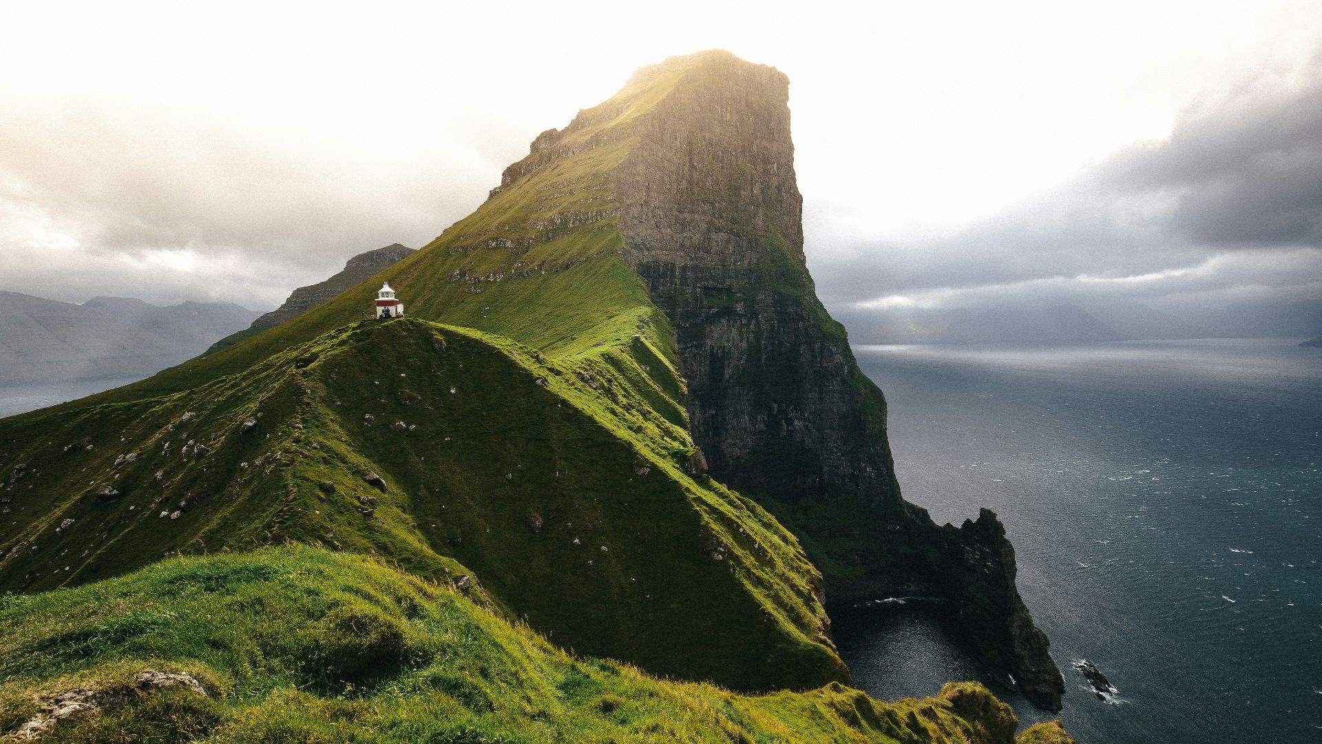 green mountain surrounded by ocean under cloudy sky during daytime
