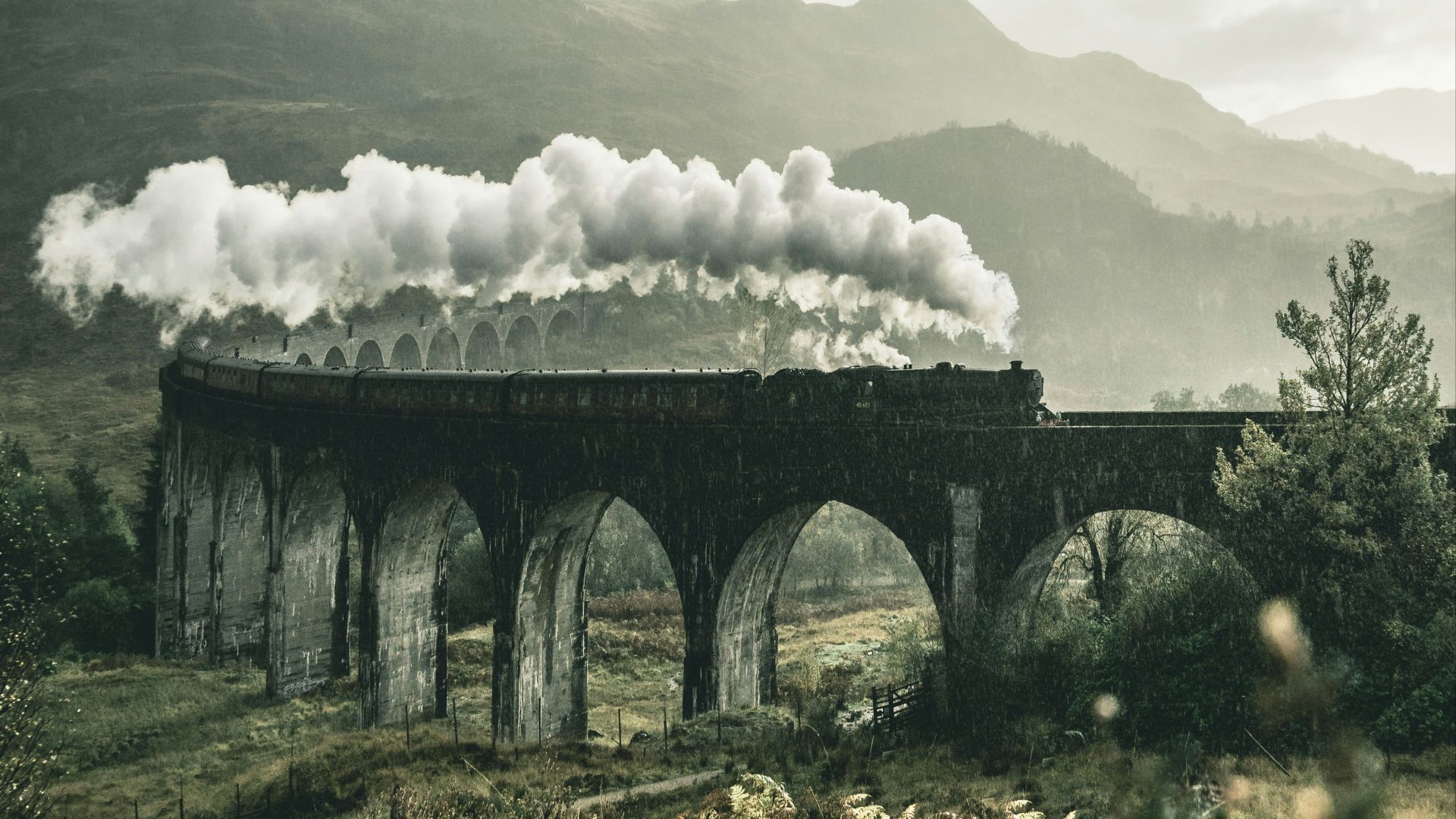 black train on railway bridge under heavy clouds