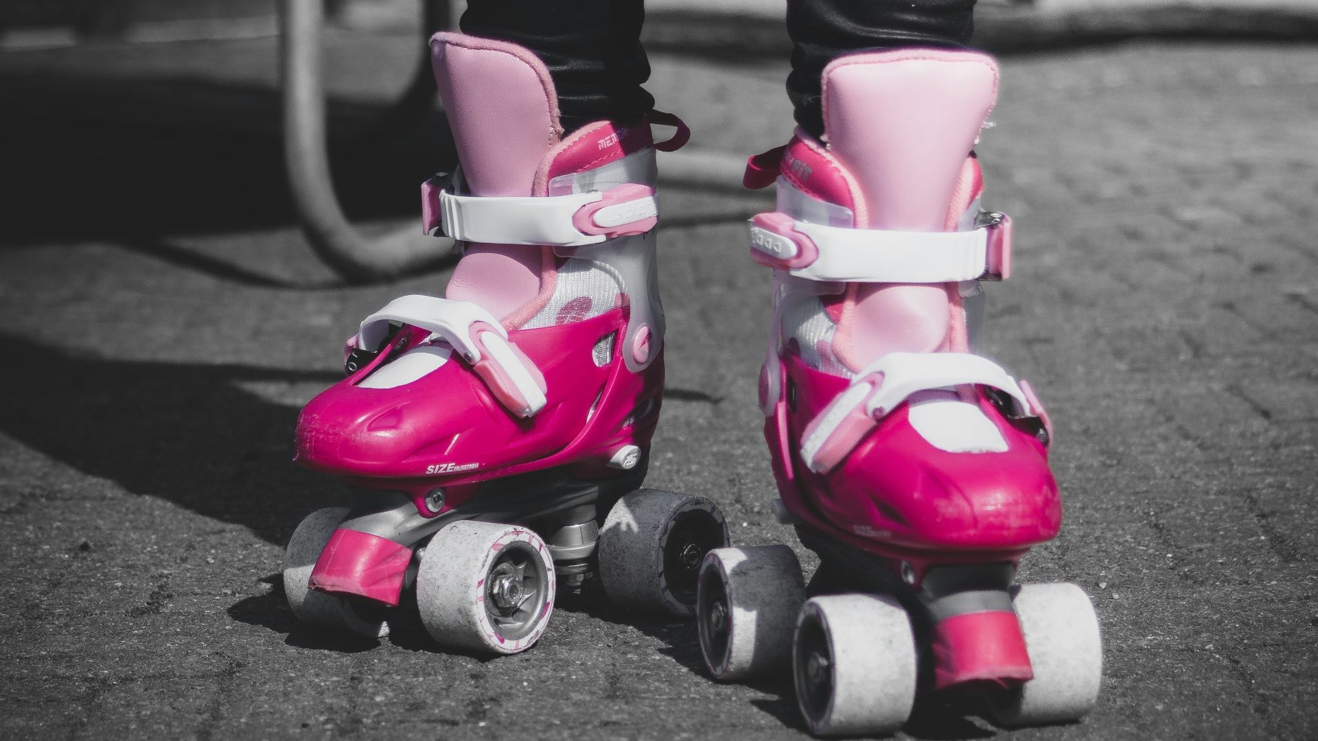 selective color photo of person wearing pair of pink roller skates
