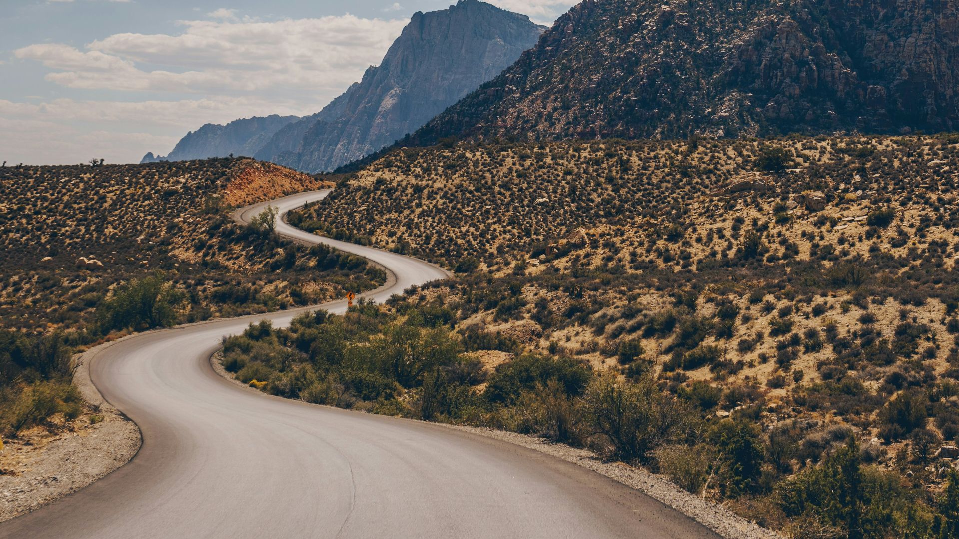 gray asphalt road between green trees and brown mountains during daytime