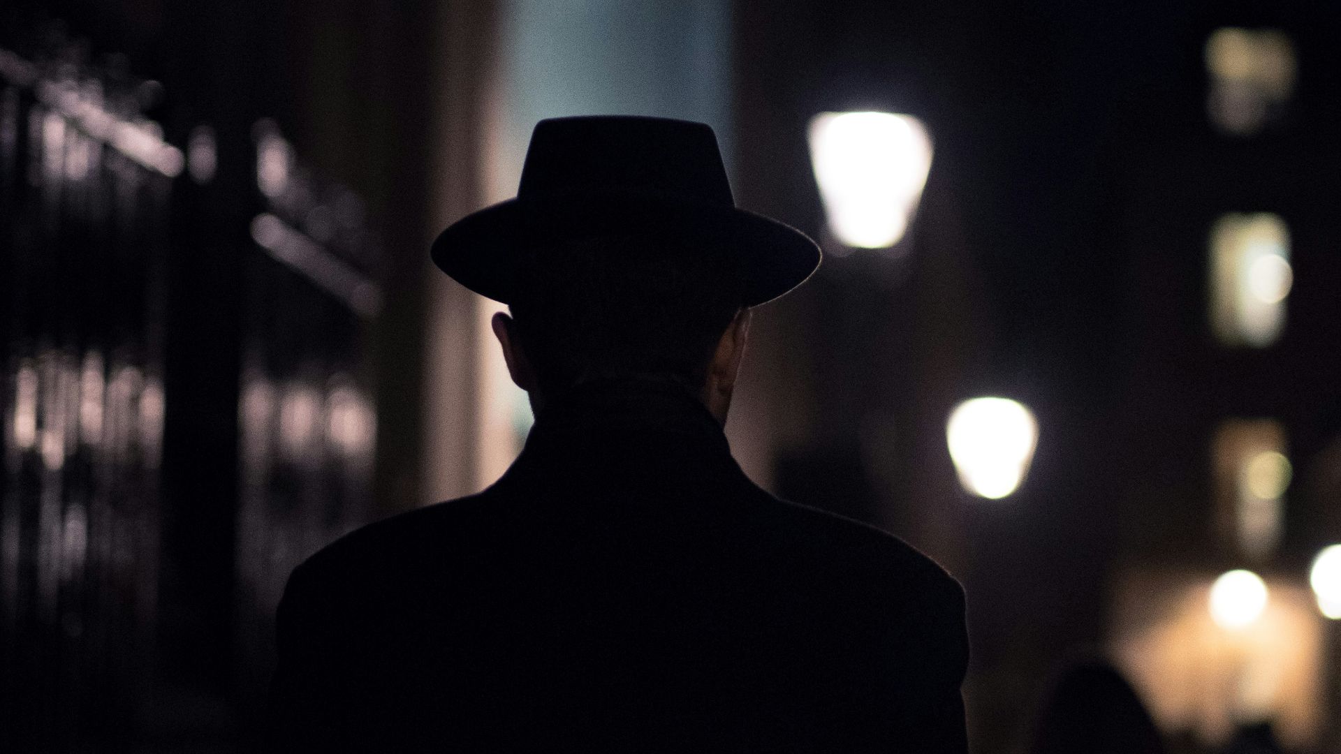 man in black hat walking on sidewalk during night time