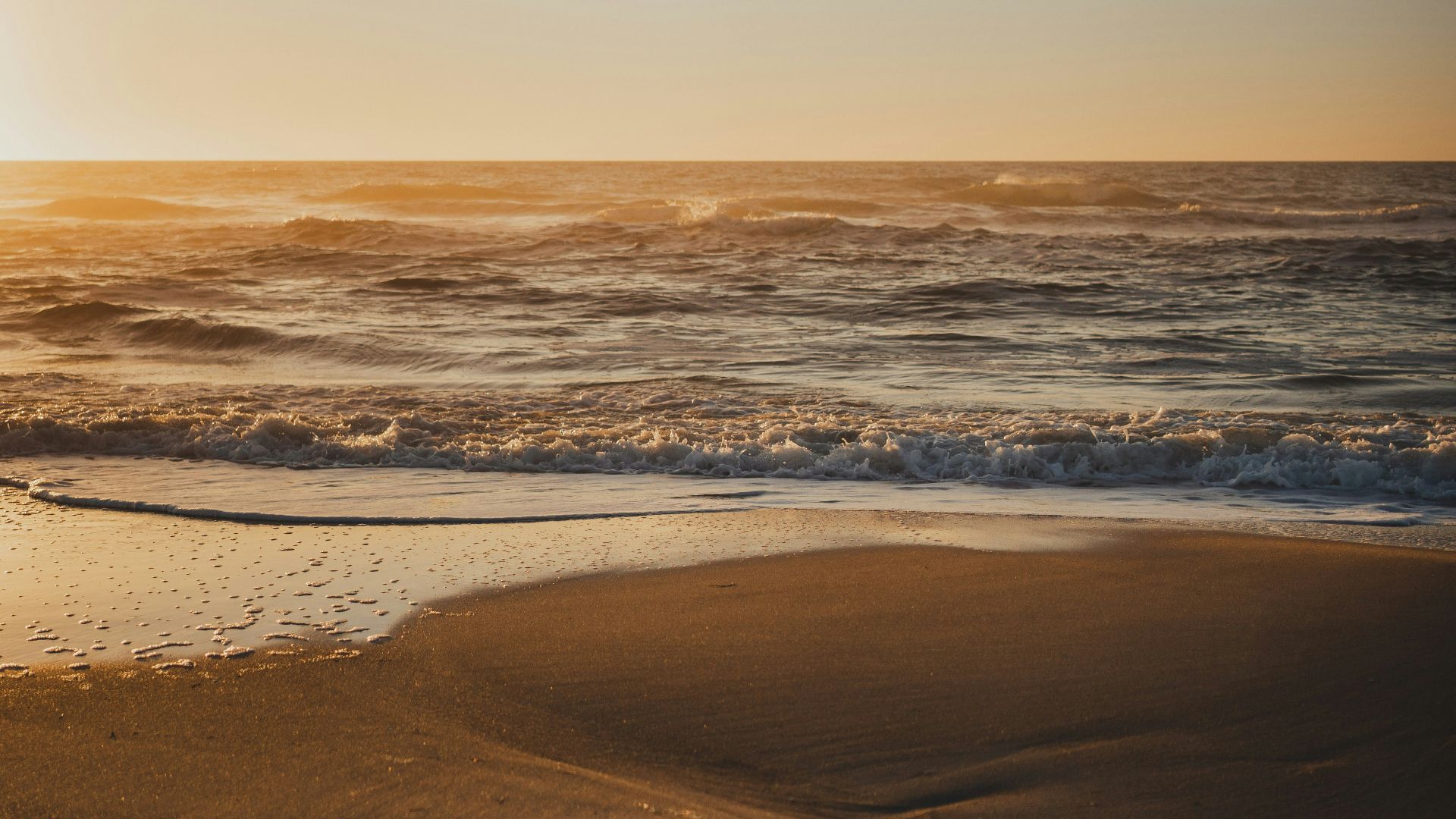the sun is setting over the ocean with footprints in the sand