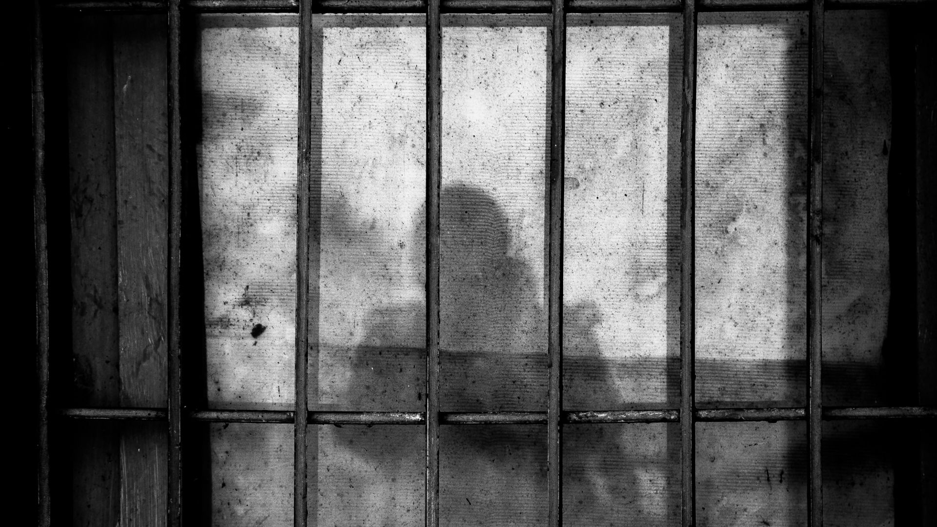 a shadow of a person behind bars in a jail cell