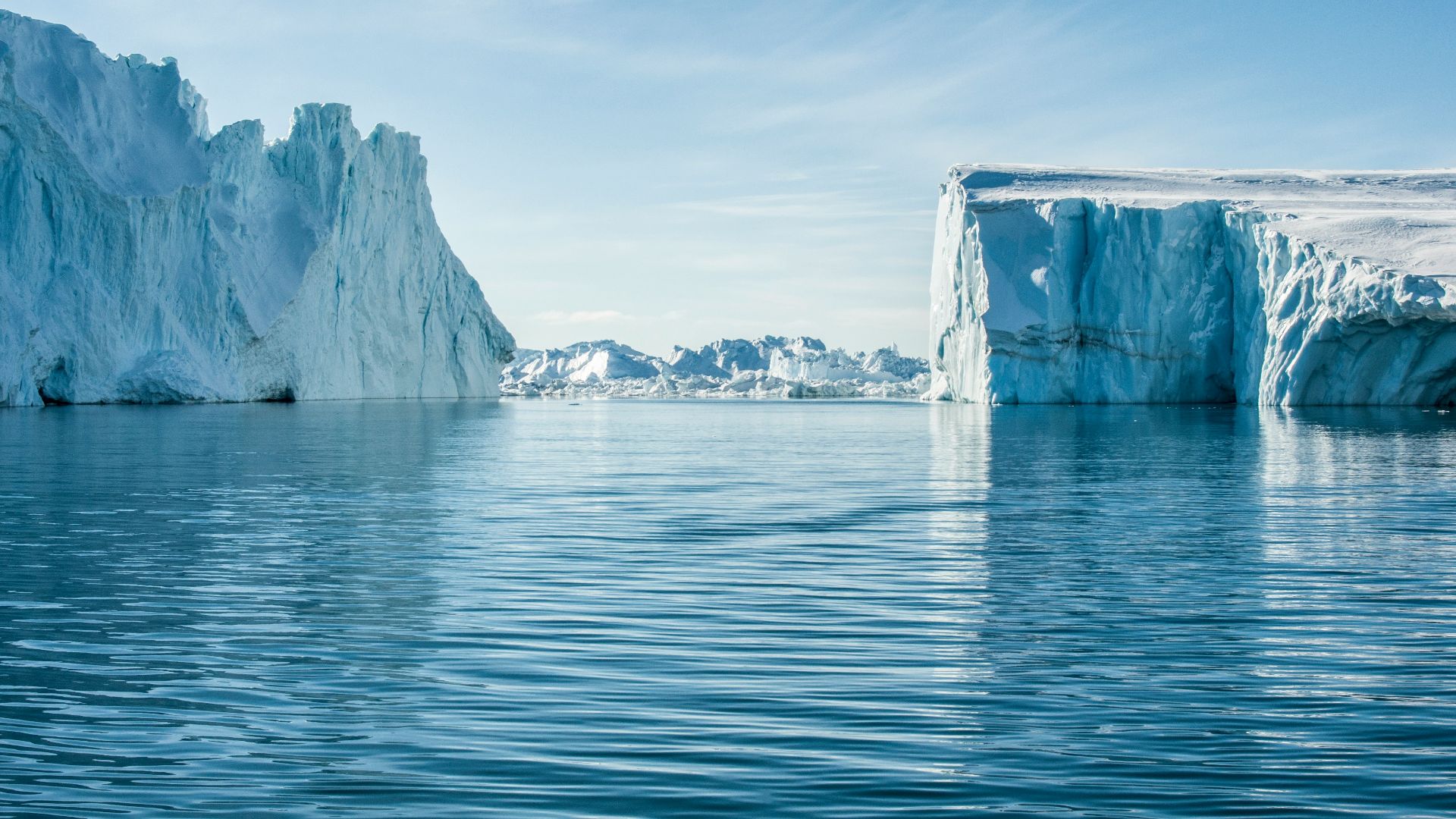 icebergs on body of water under blue and white sky at daytime