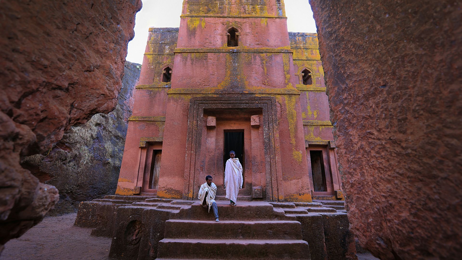 person in white dress in front of pink building