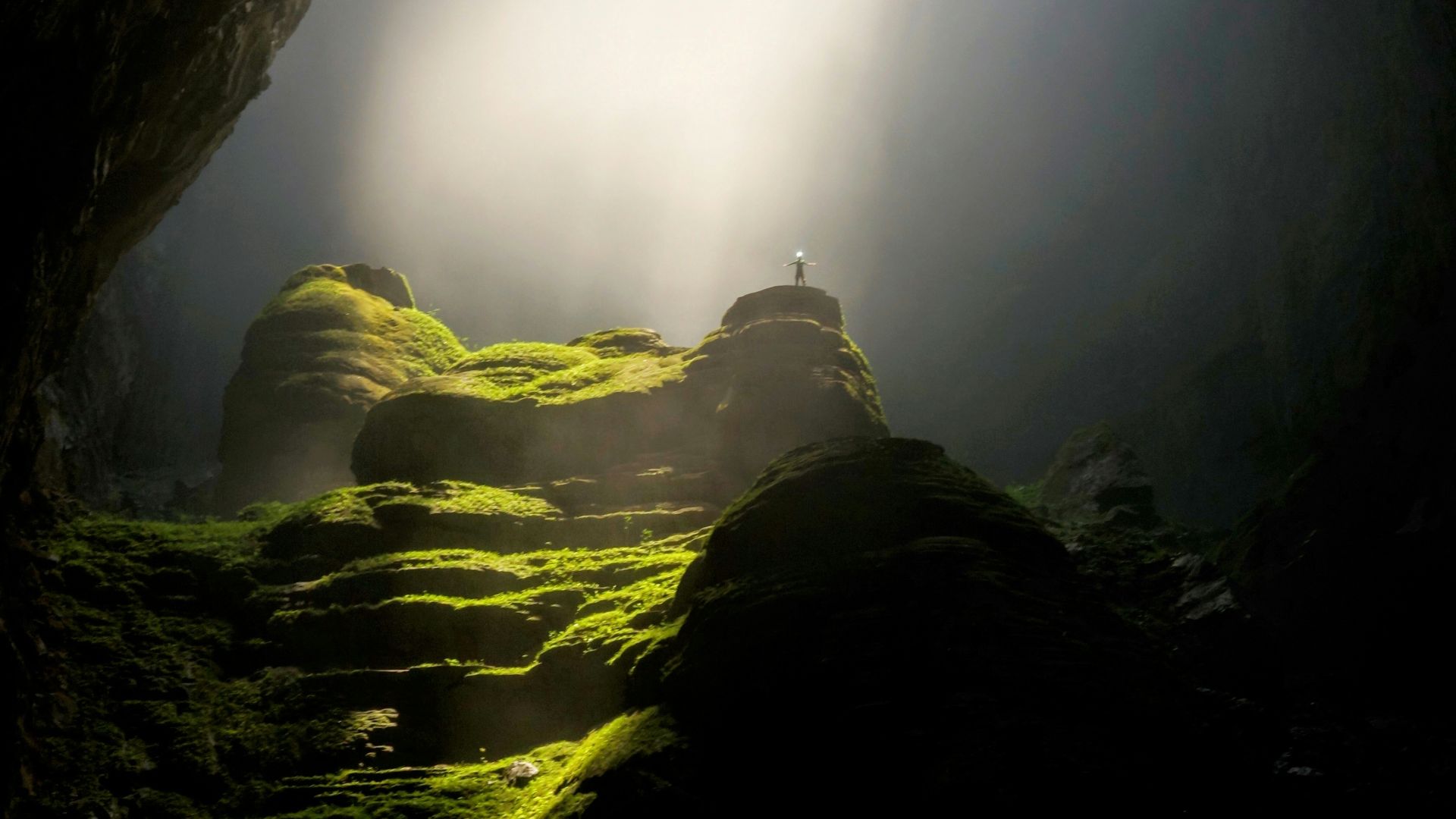 person on top of rock formation inside cave