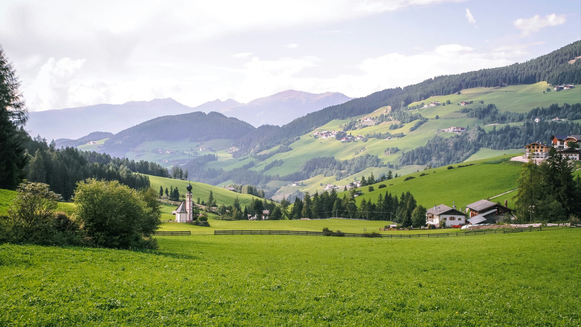 green grass field near green mountains under white clouds during daytime