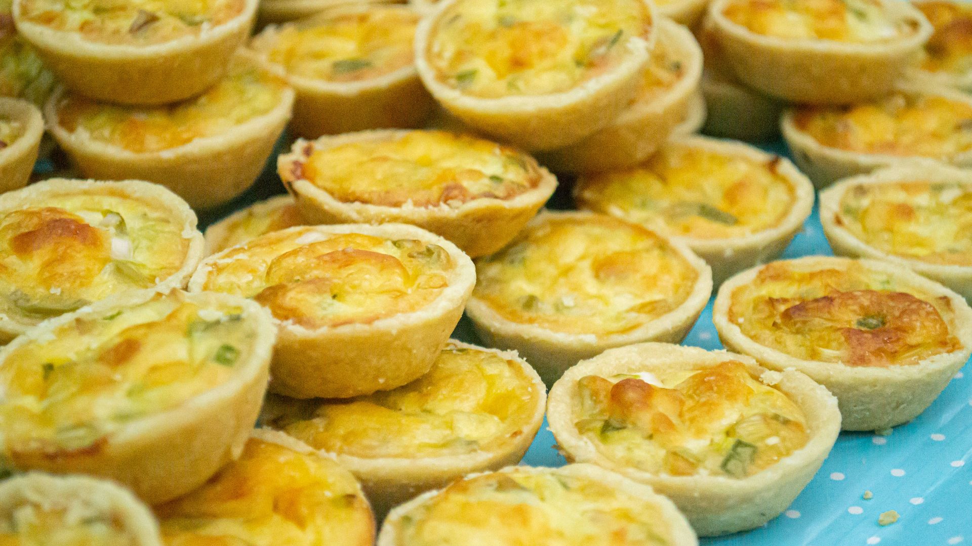 a table topped with mini quiches on top of a blue table cloth