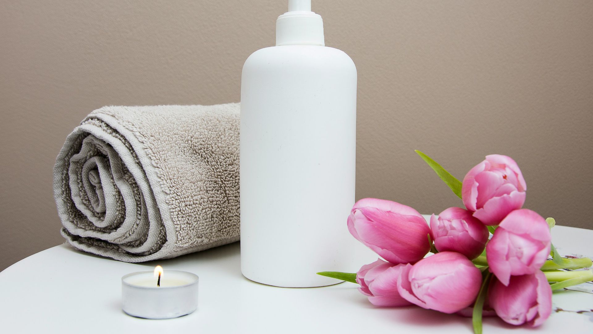 white plastic pump bottle beside pink tulips and gray towel