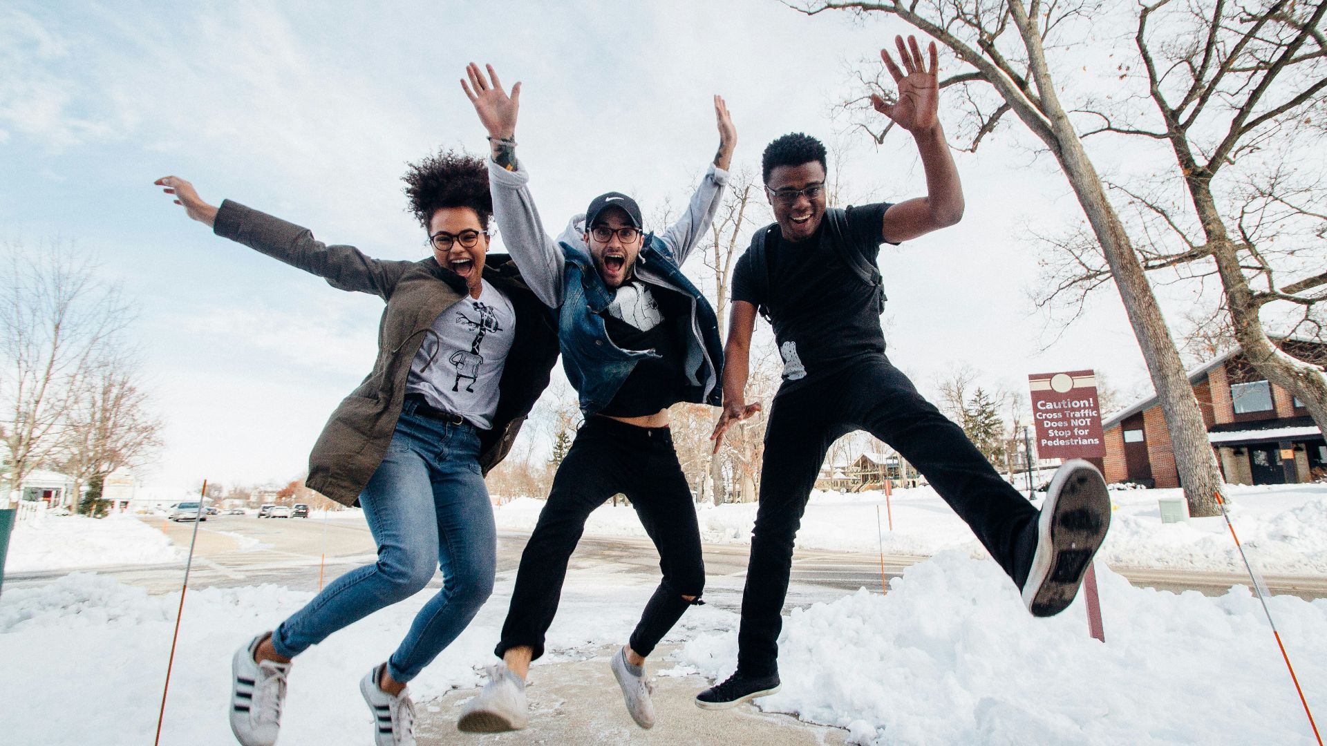 photo of three men jumping on ground near bare trees during daytime