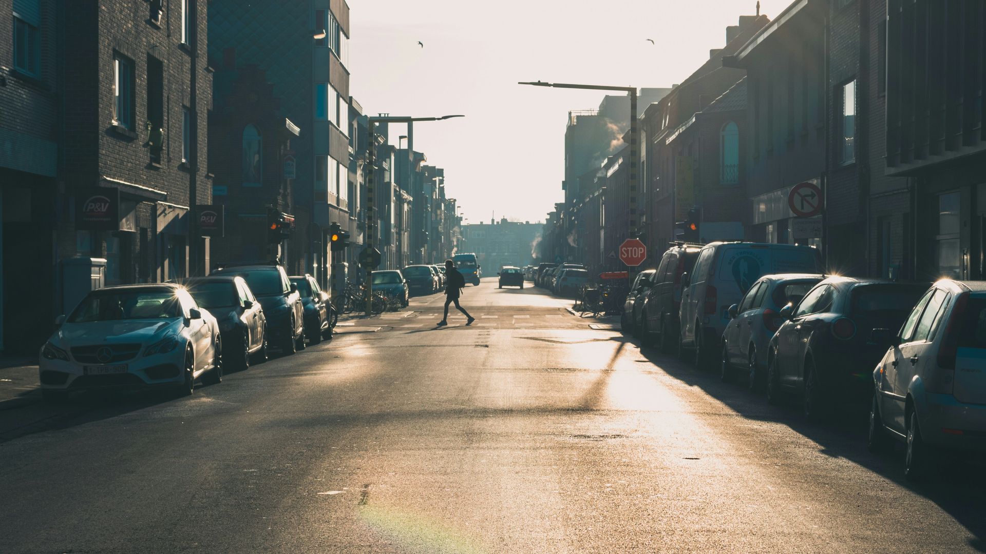 a person walking down a street next to parked cars