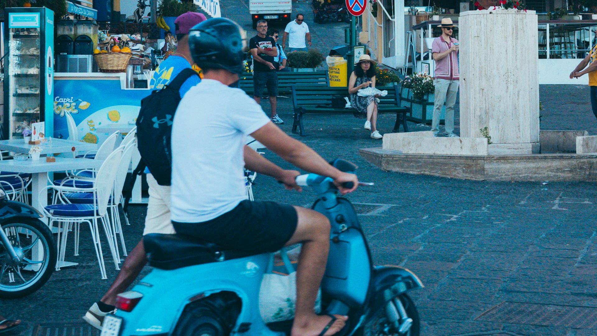 People ride scooters past buildings decorated with italian flags.