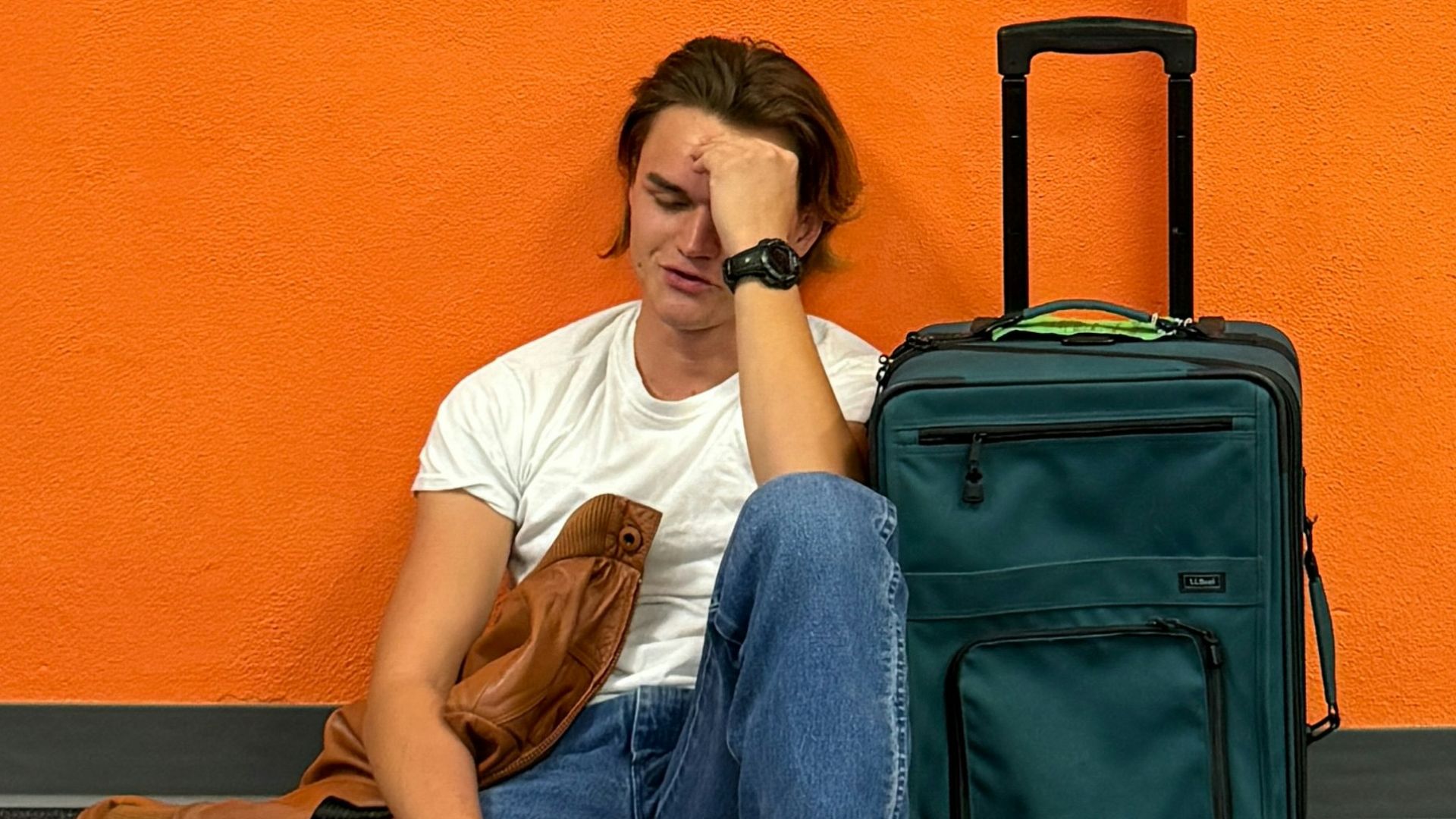 Man sitting on floor with luggage, looking tired.