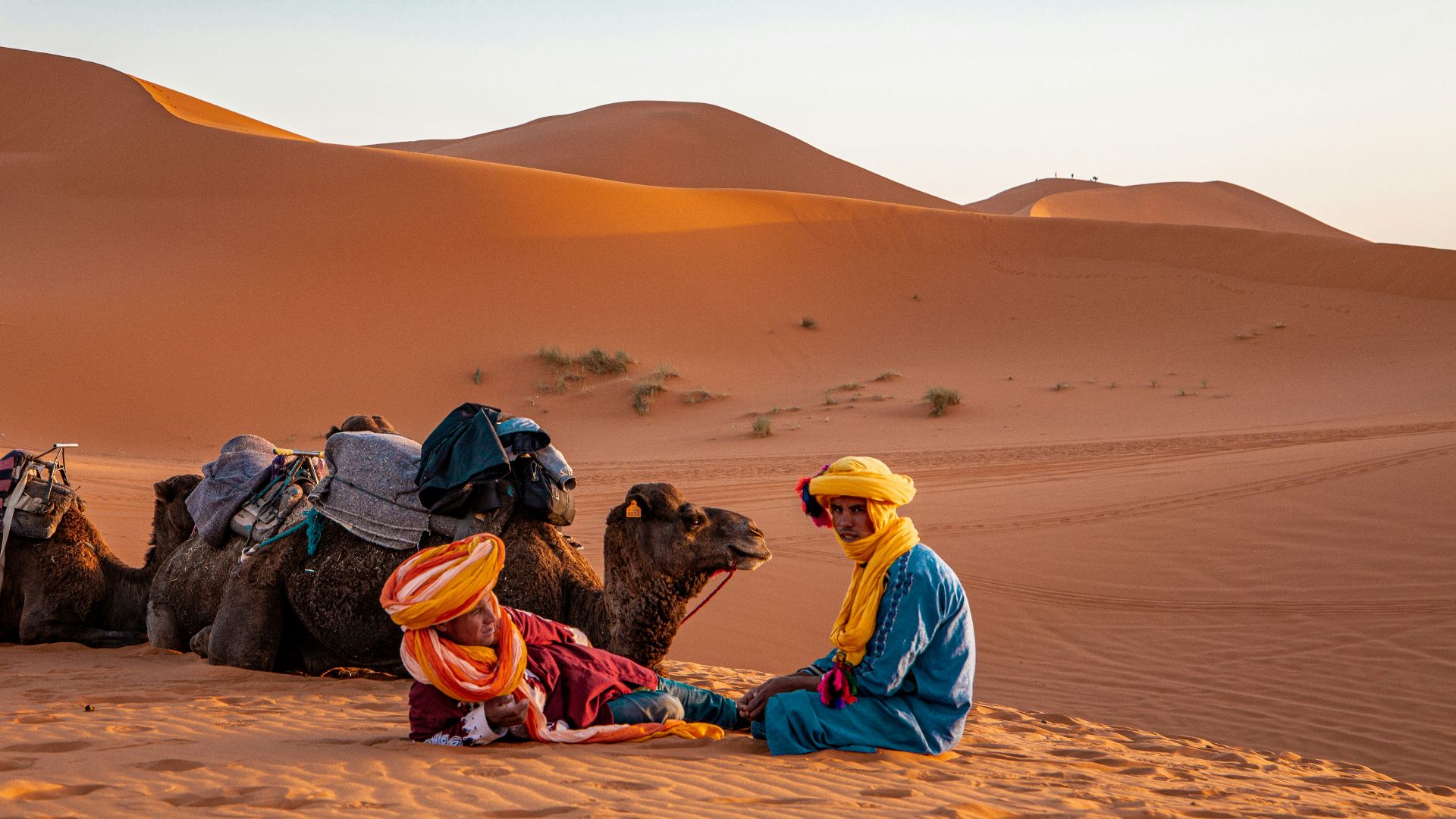 man in yellow robe sitting on brown sand during daytime