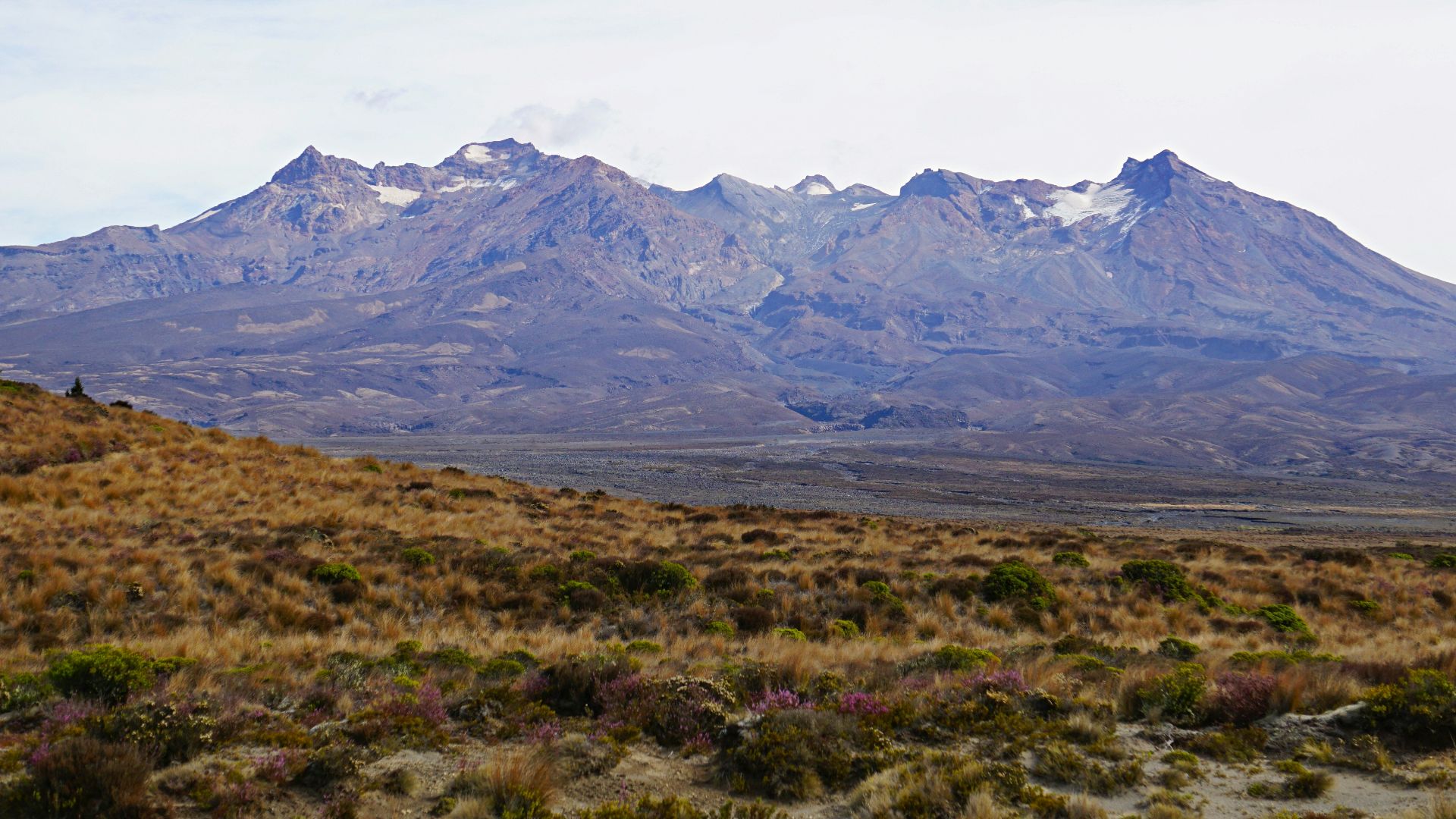 green grass field near mountain under white clouds during daytime