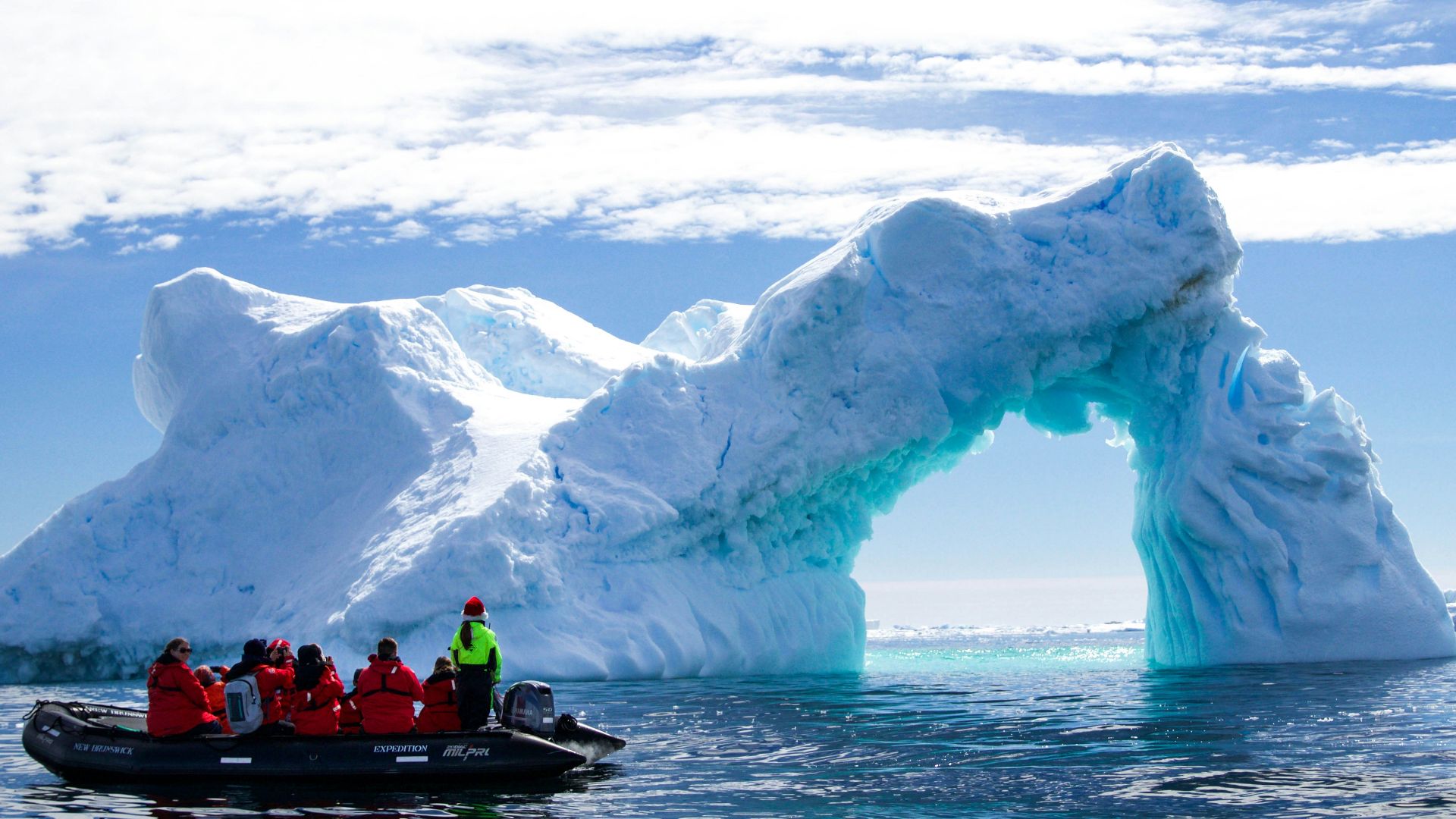 a group of people in a small boat in front of an iceberg
