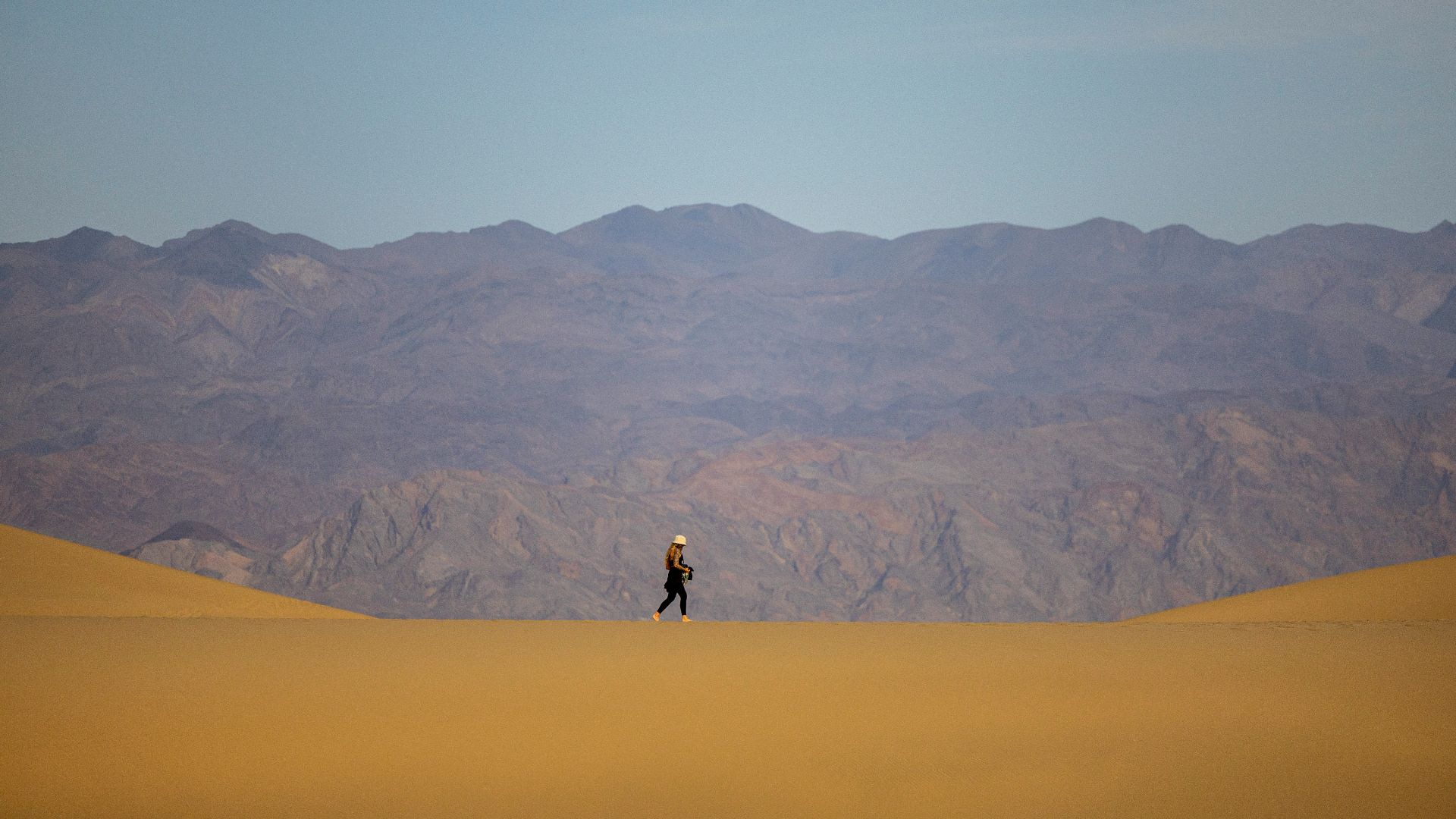a person walking across a desert with mountains in the background