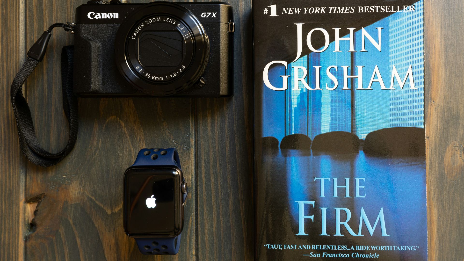 Canon G7X camera beside Apple Watch and The Frim by John Grisham book