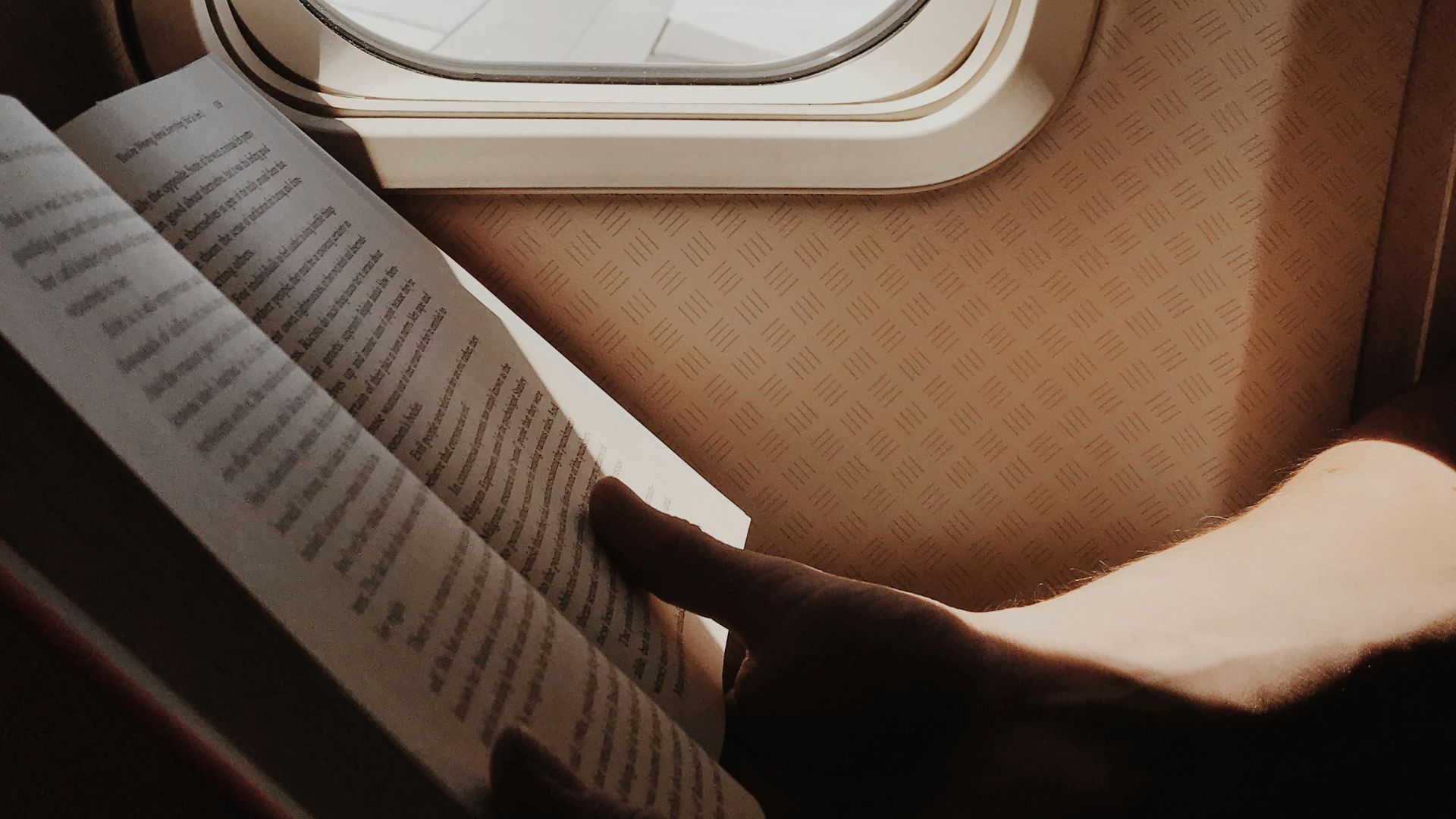person reading book beside airplane window