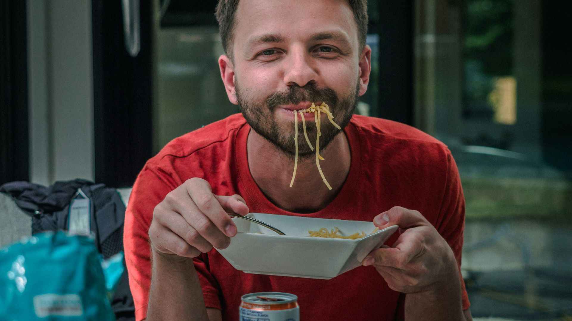 man in red crew neck t-shirt holding white and red labeled can