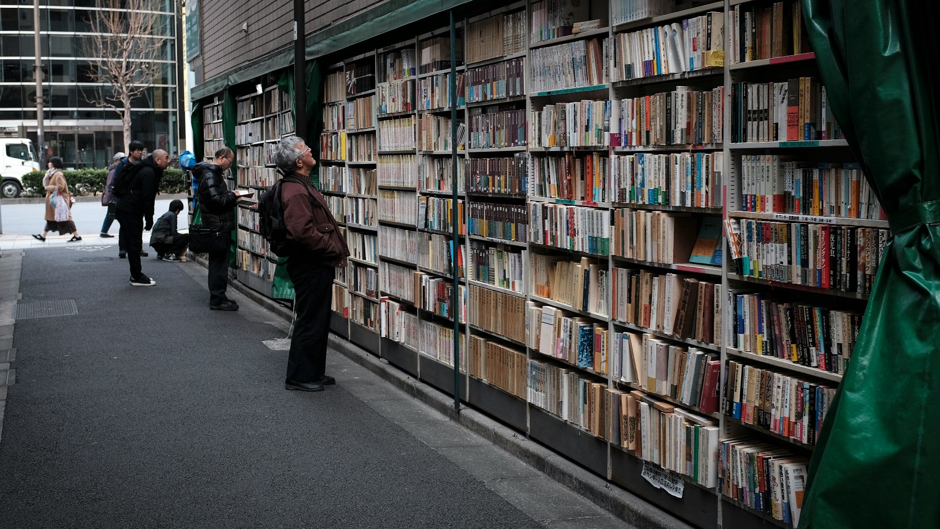 man in black jacket standing near books in book shelves