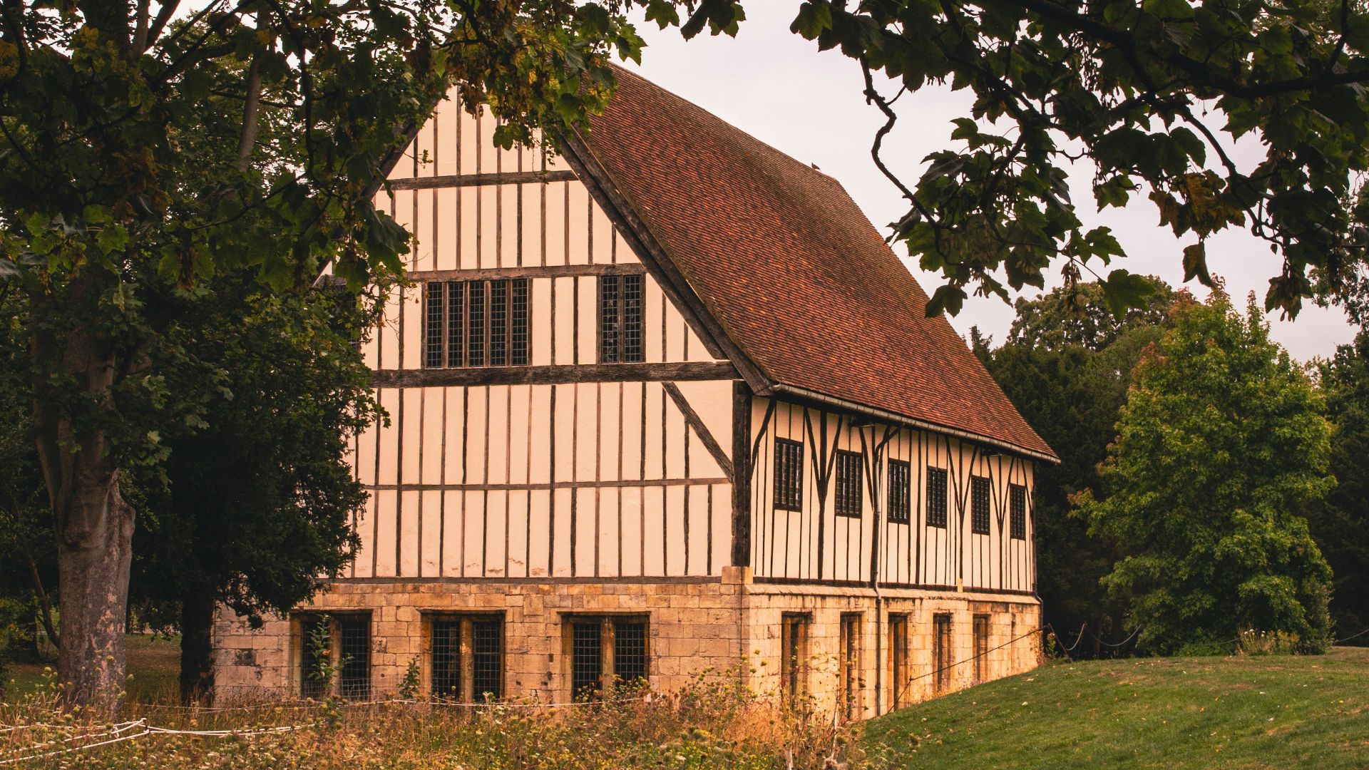 Timber-framed building with red tile roof in grassy field.