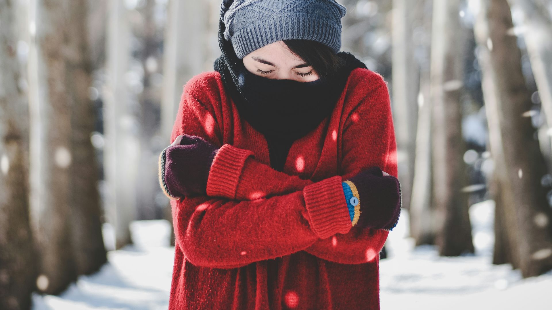 person in red jacket wearing blue knit cap standing near snow covered trees during daytime
