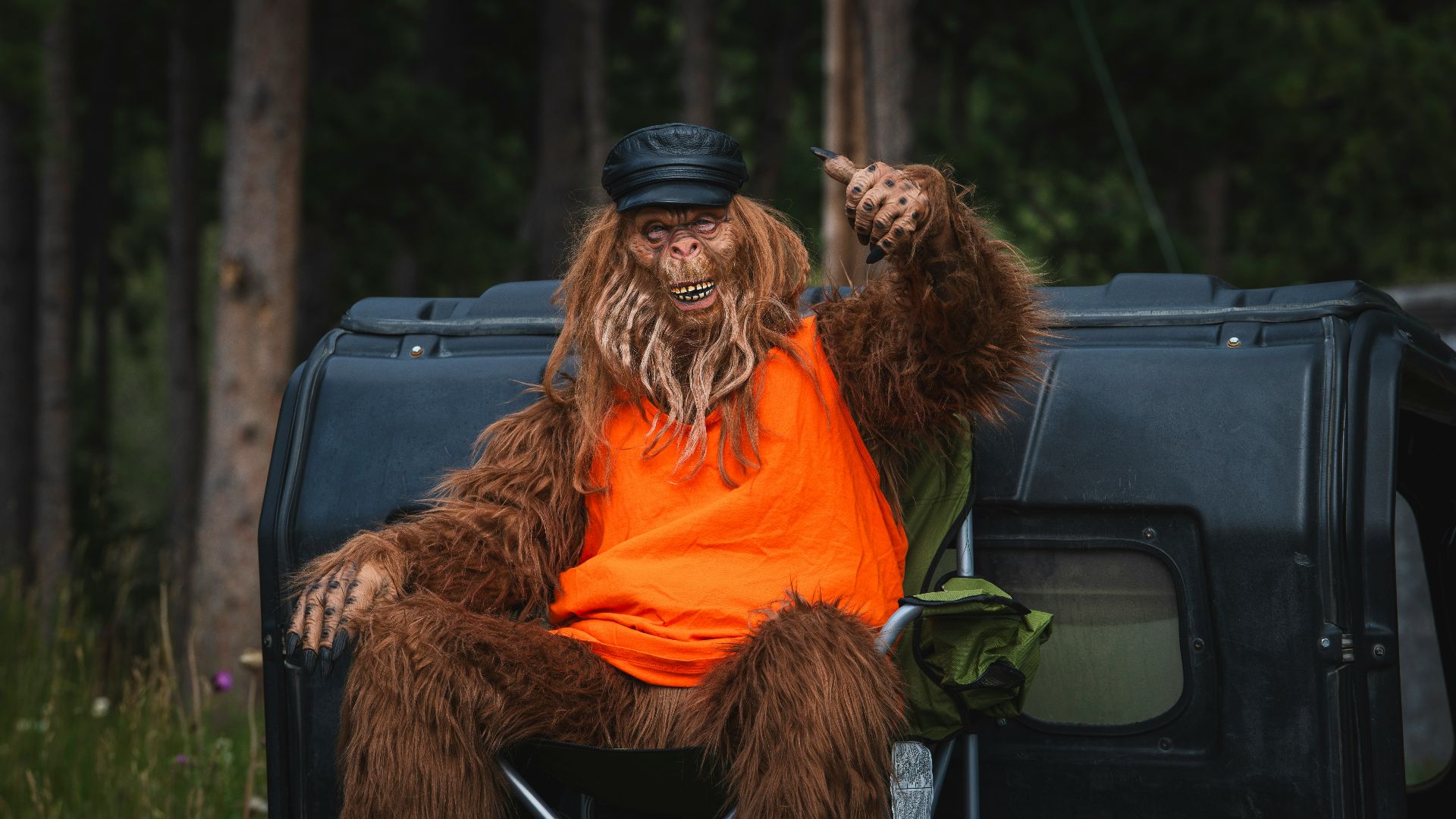 Bigfoot is relaxing by a car in the woods.