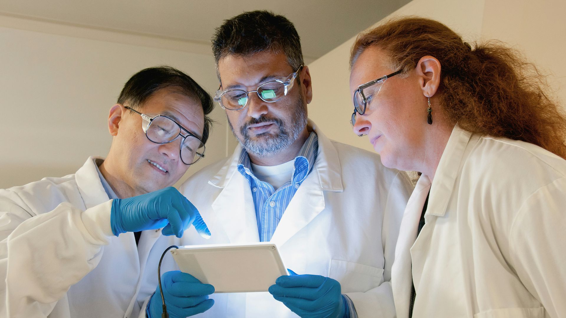three people in lab coats looking at a tablet