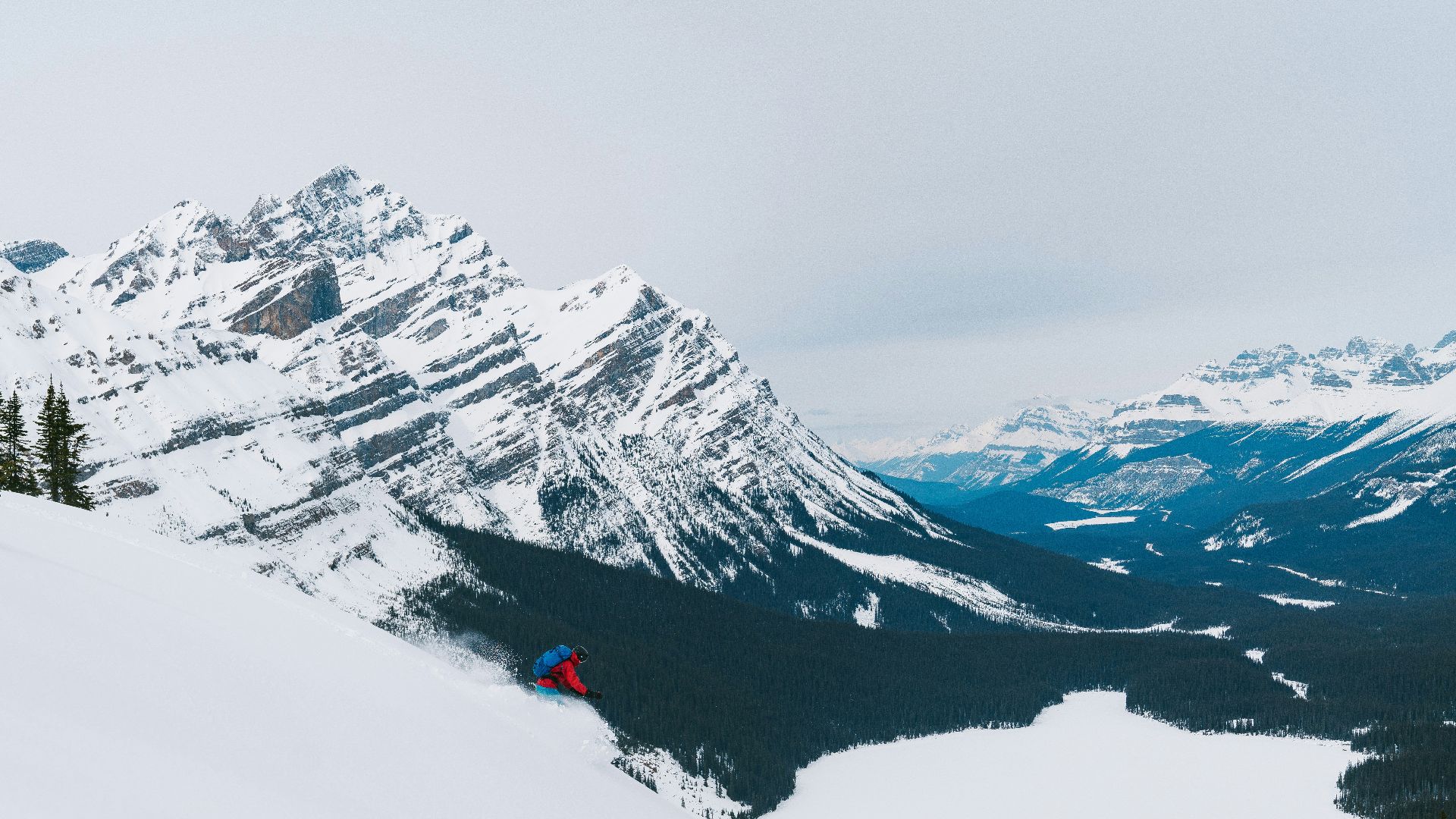 person in red jacket and black pants standing on snow covered ground near snow covered mountain