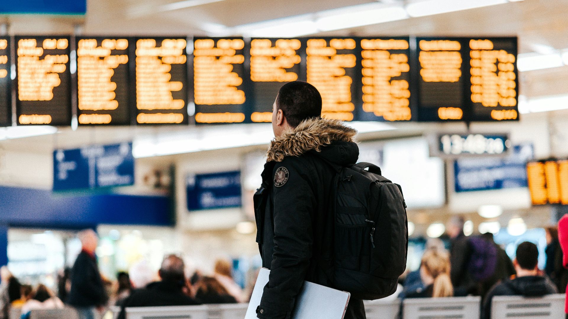 man standing inside airport looking at LED flight schedule bulletin board