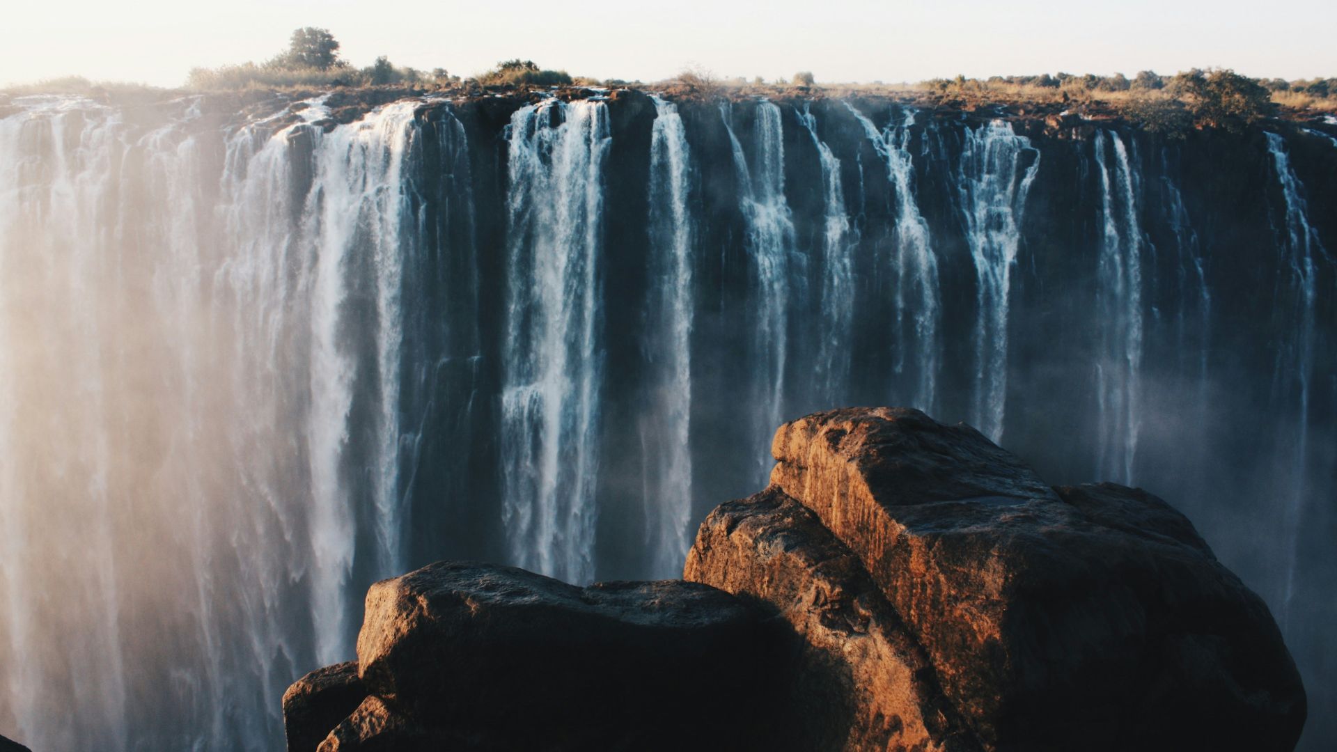 water falls on brown rocky mountain during daytime
