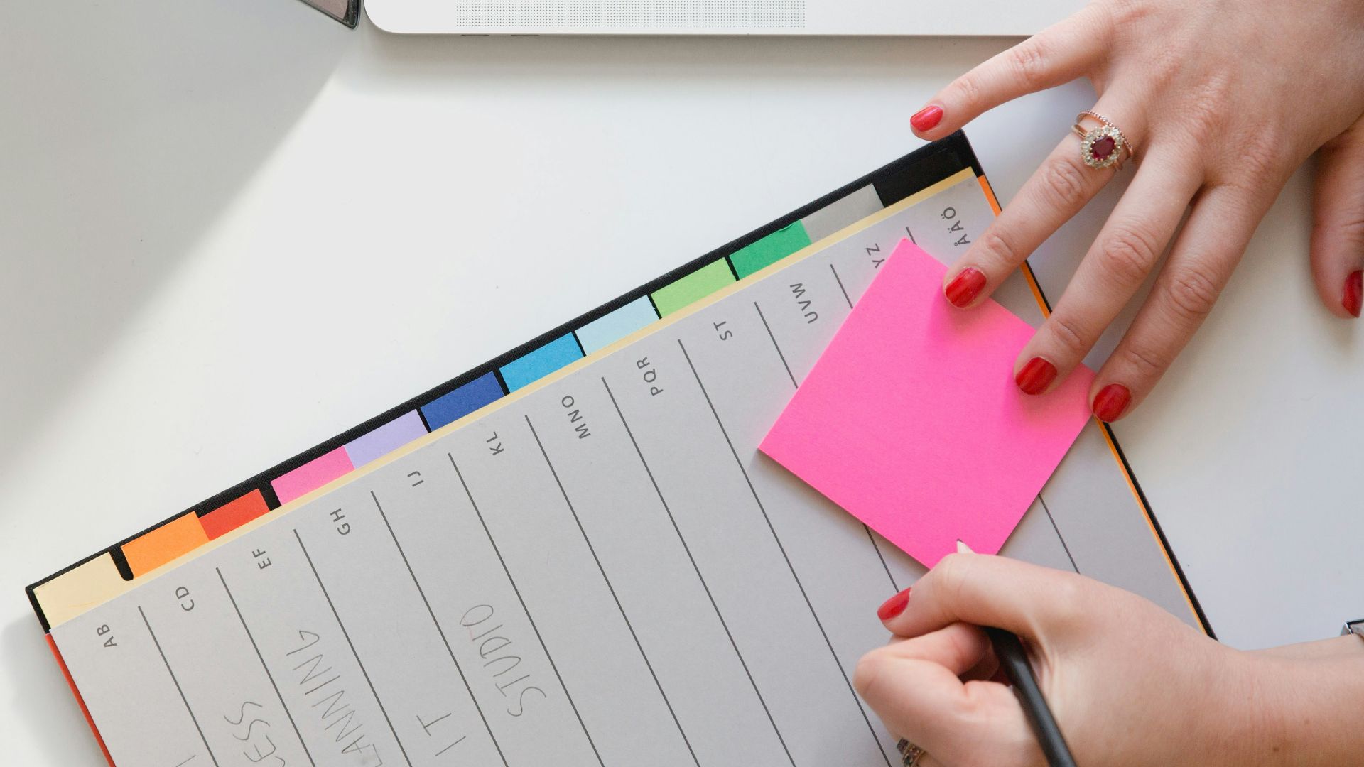 person holding pencil and stick note beside table