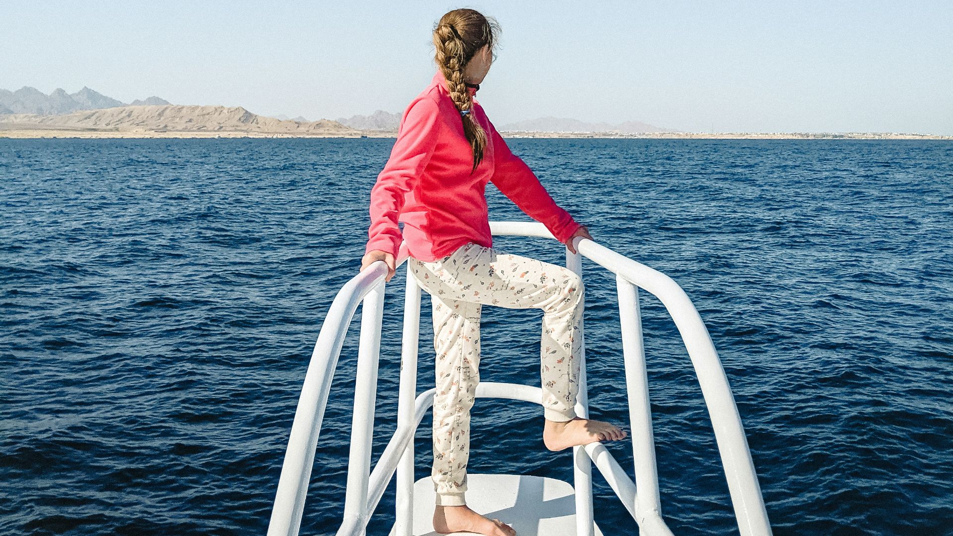 woman in red dress standing on white metal railings near body of water during daytime