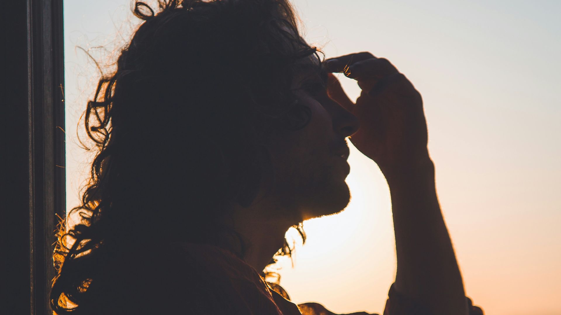 man holding forehead under sunset