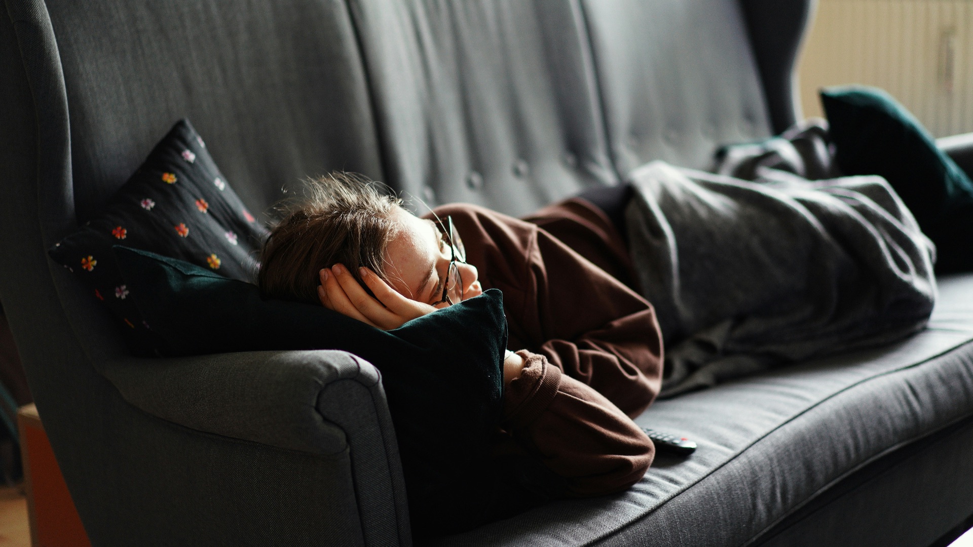 woman in pink jacket lying on gray couch
